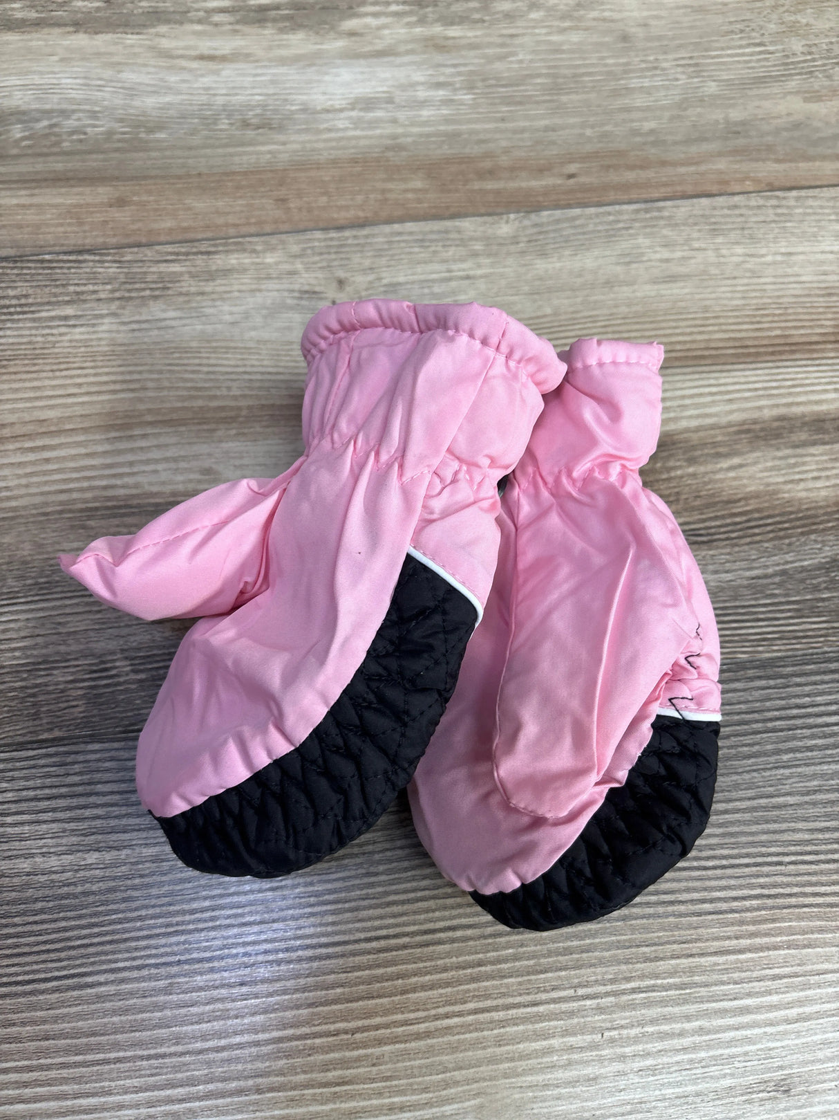Pair of pink and black quilted toddler mittens on wood surface for kids winter wear