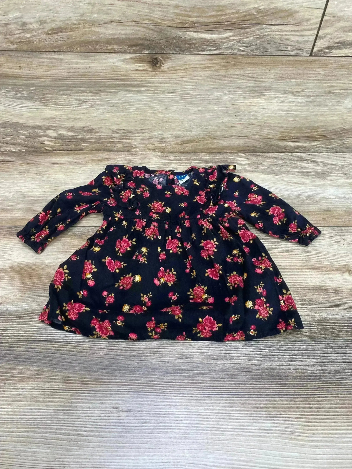 Flat lay of Old Navy 0-3M black floral ruffle dress showing ruffle neckline, long sleeves, gathered waist on light wood floor