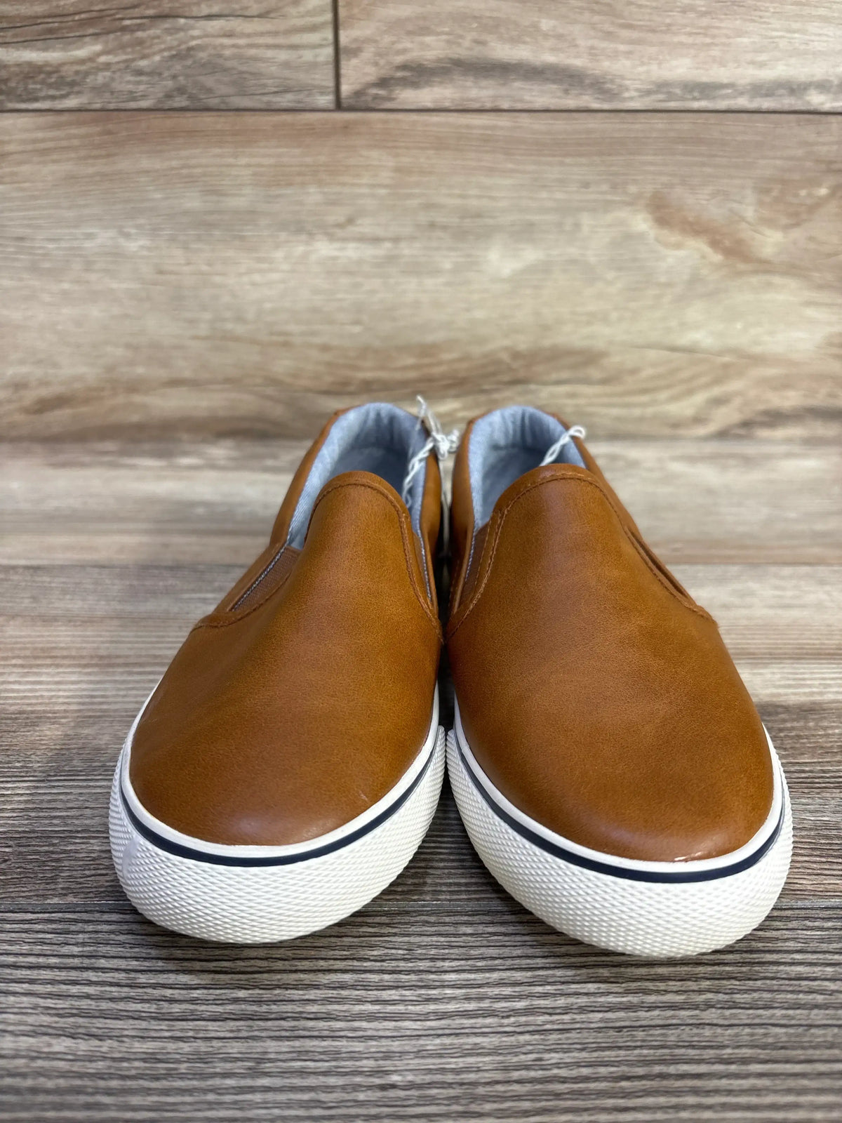 Front view of Cat & Jack Enzo slip-on sneakers with brown faux-leather upper and white platform sole on wood