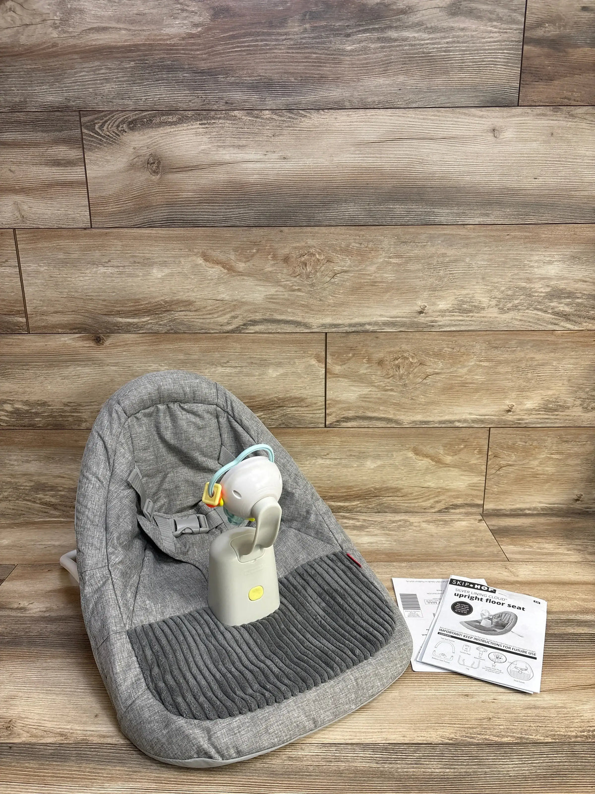 Gray Skip Hop upright floor seat for babies, with toy attachment and instruction manual on wood floor.