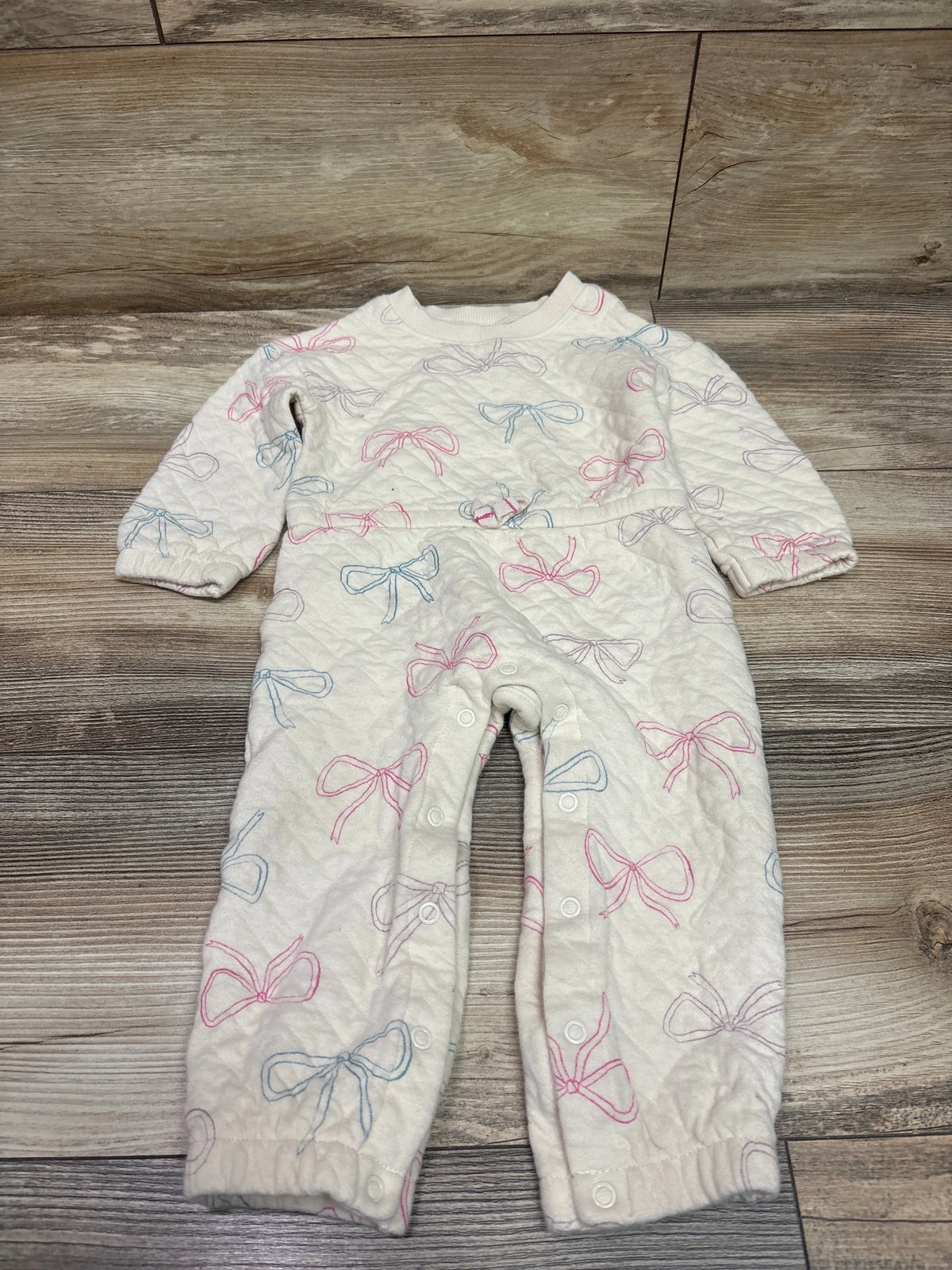 Front view of Carter’s beige quilted coverall in size 18 months showcasing bow pattern and snap closures on wood floor