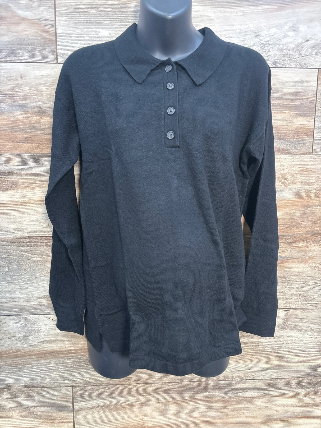 Black long sleeve knit polo shirt with four buttons on mannequin, wood background