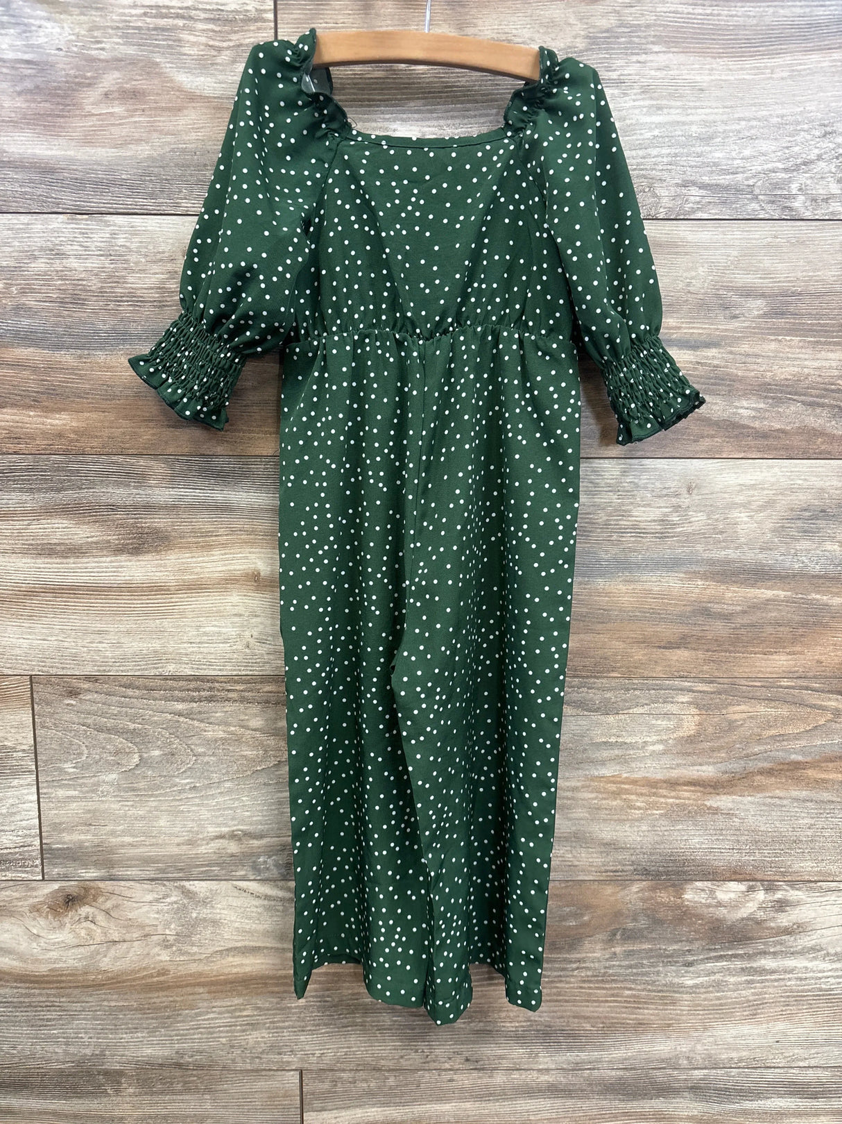 Front view of emerald green polka dot 2T romper showing smocked bodice, ruffled neckline and smocked sleeve cuffs on wood background