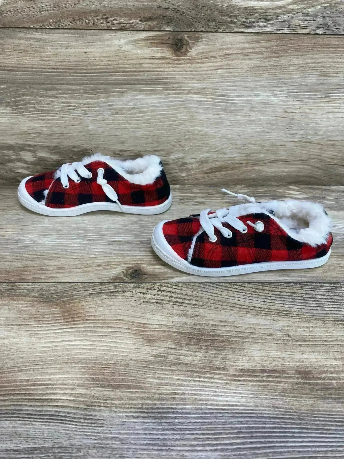 Side view of toddler slip-on sneakers size 10C with red and black buffalo plaid upper and white faux-fur lining on wood background