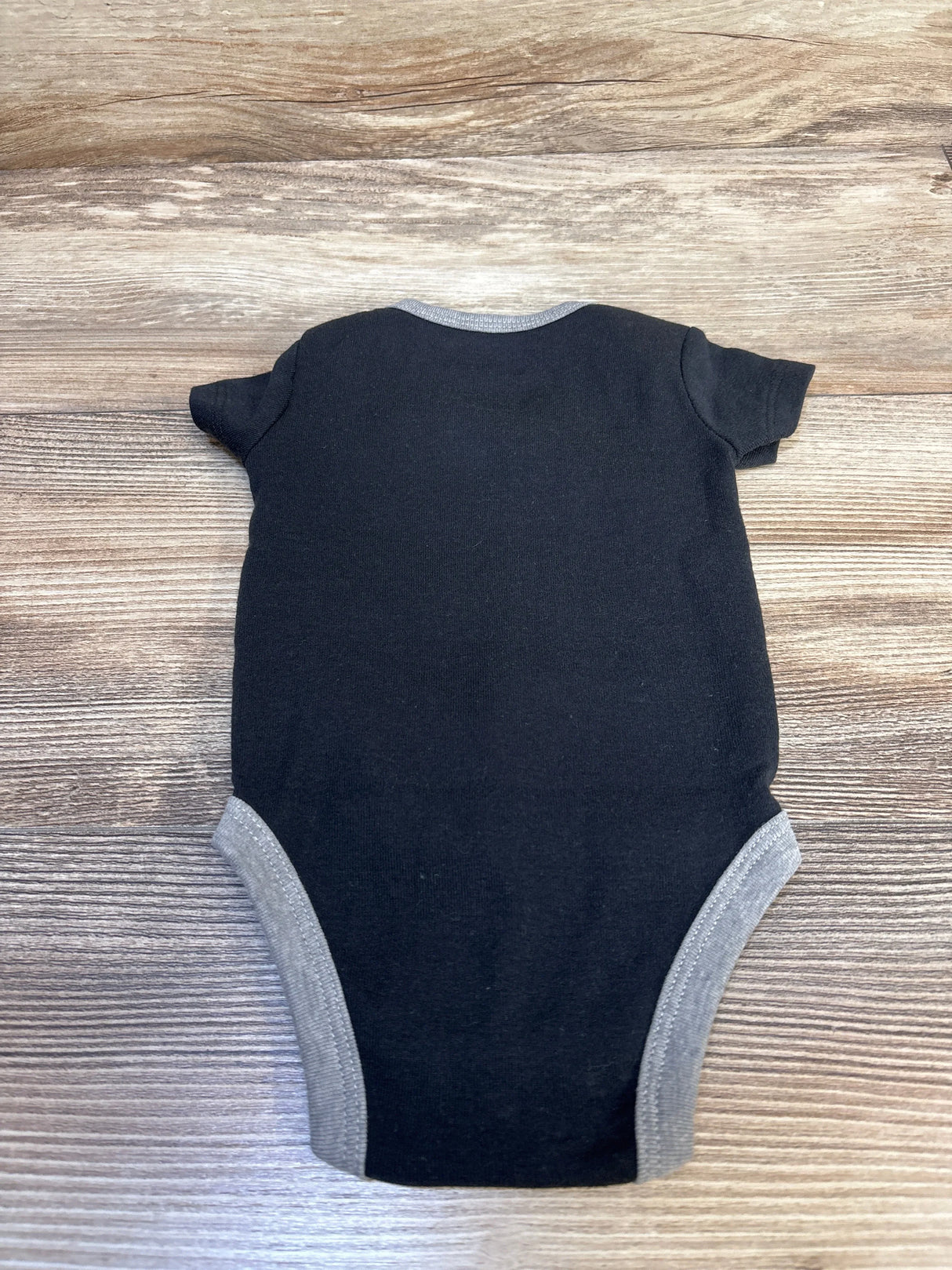 Top-down view of Nike newborn black bodysuit showing short sleeves and gray trim at neck and leg openings on wood background