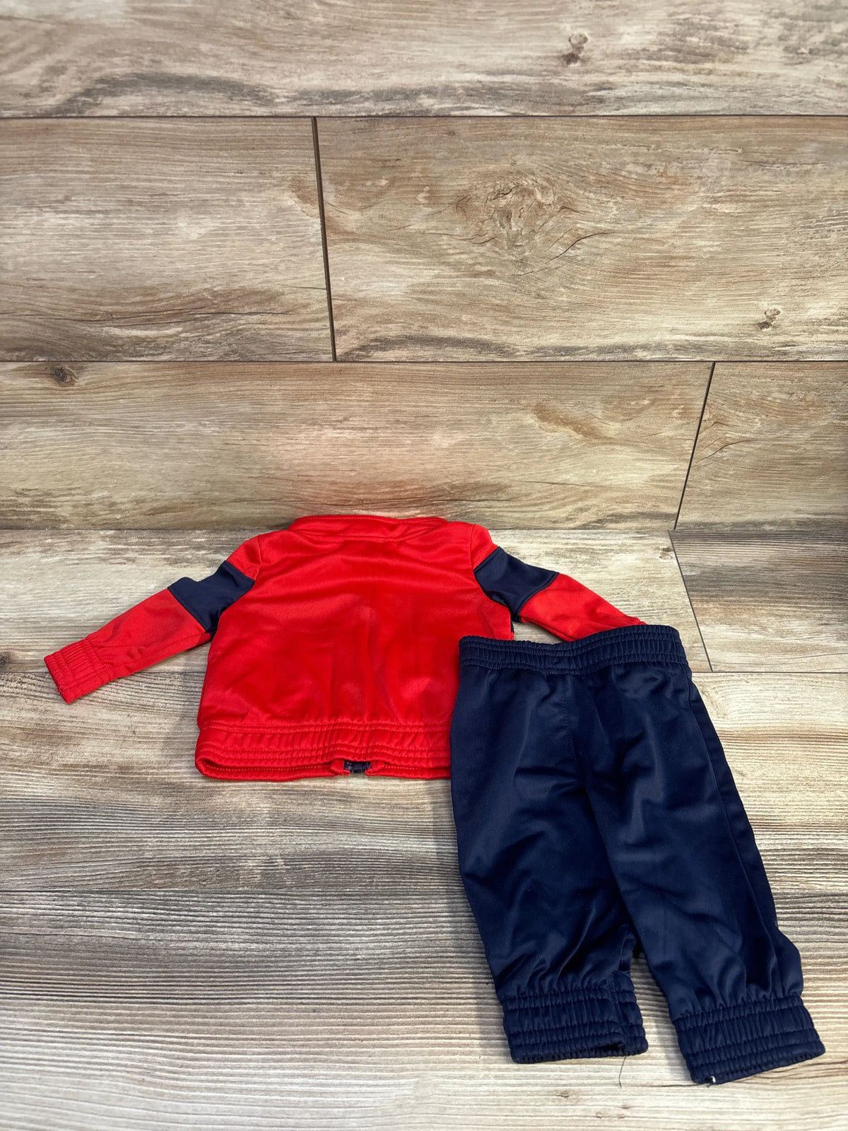 Back view of newborn 0-3M Puma red 2-piece tracksuit with navy pants showing elastic cuffs and waist on wood background