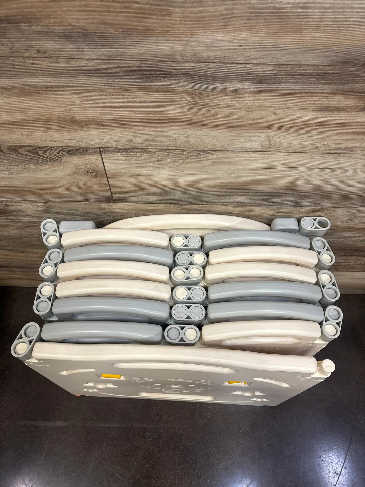 Overhead view of UANLAUO Foldable 14-Panel Playpen showcasing folded gray and cream panels on a wood floor