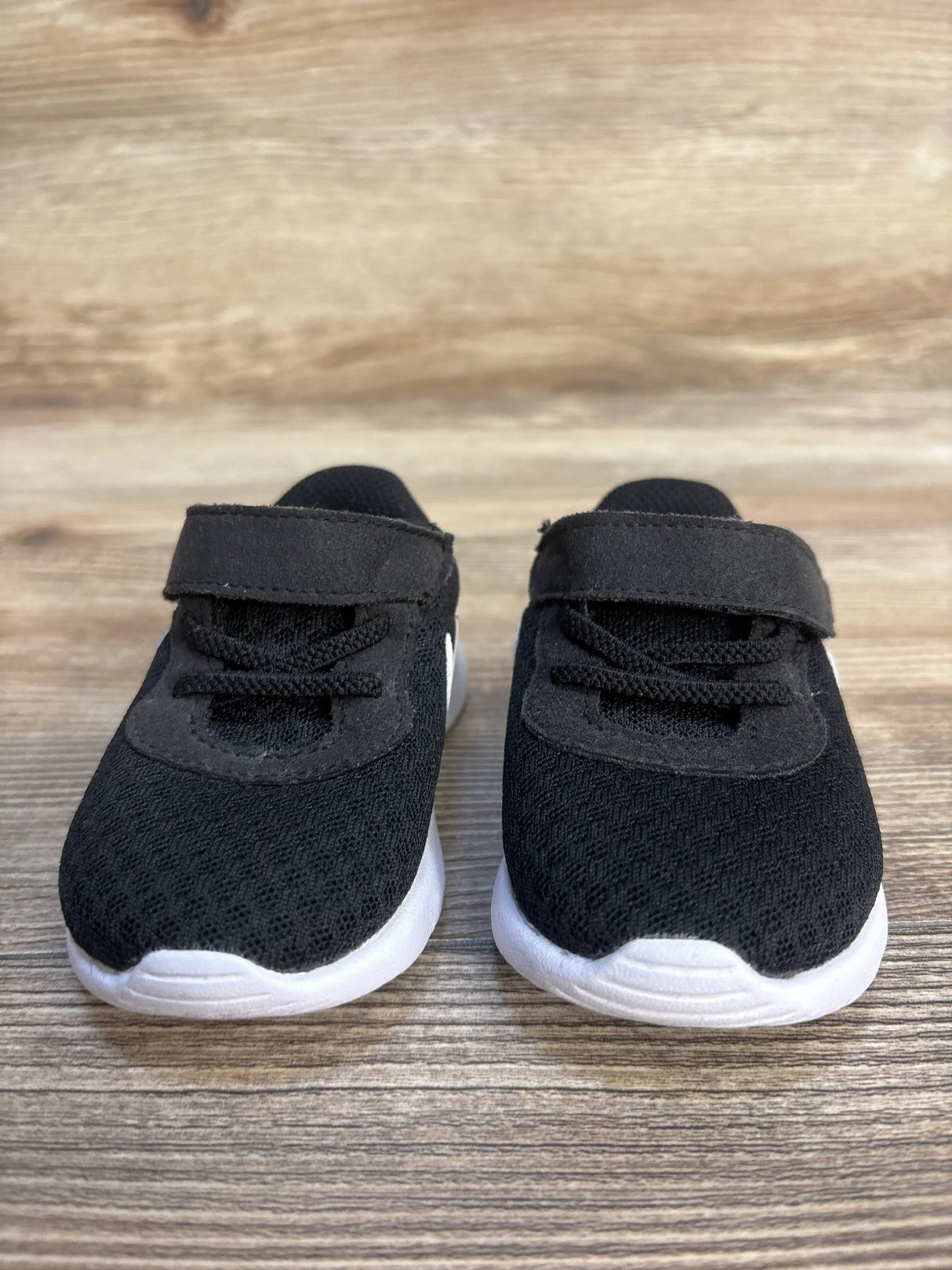 Pair of black toddler sneakers with white soles on wood surface