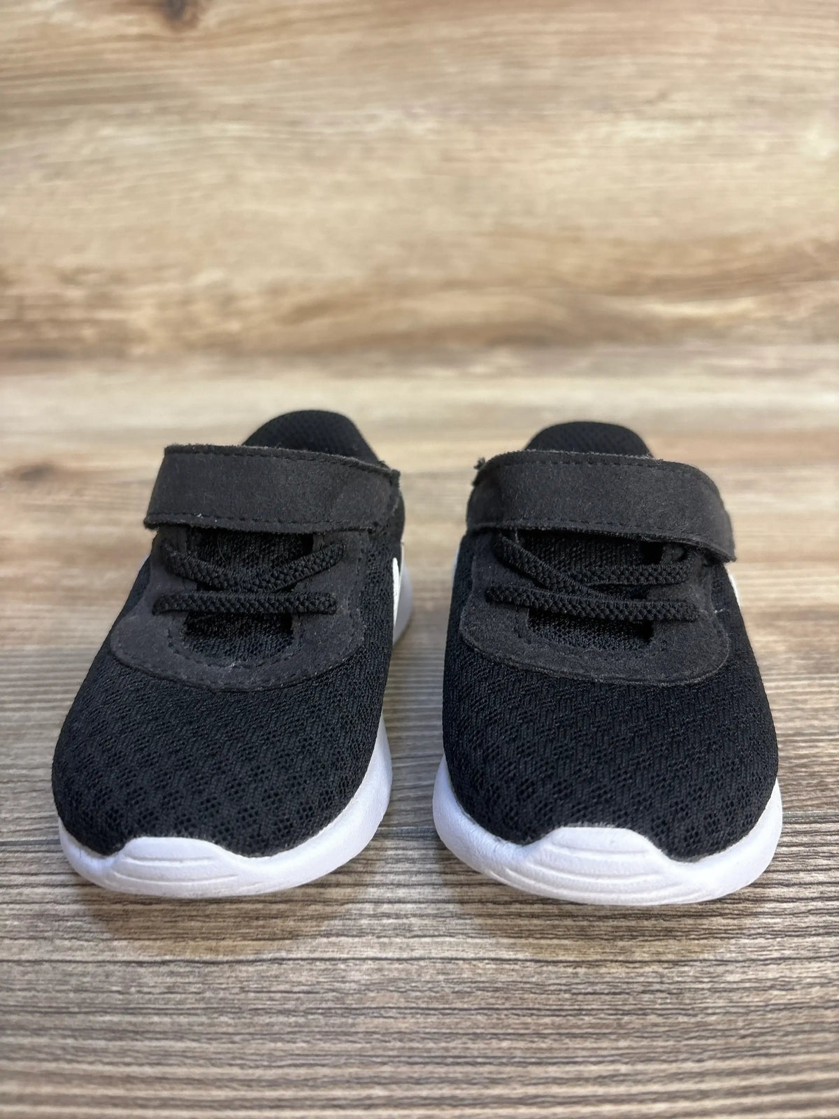 Front view of Nike Tanjun TDV toddler sneakers size 4C showcasing black mesh upper, hook and loop strap, and white soles on a wood surface