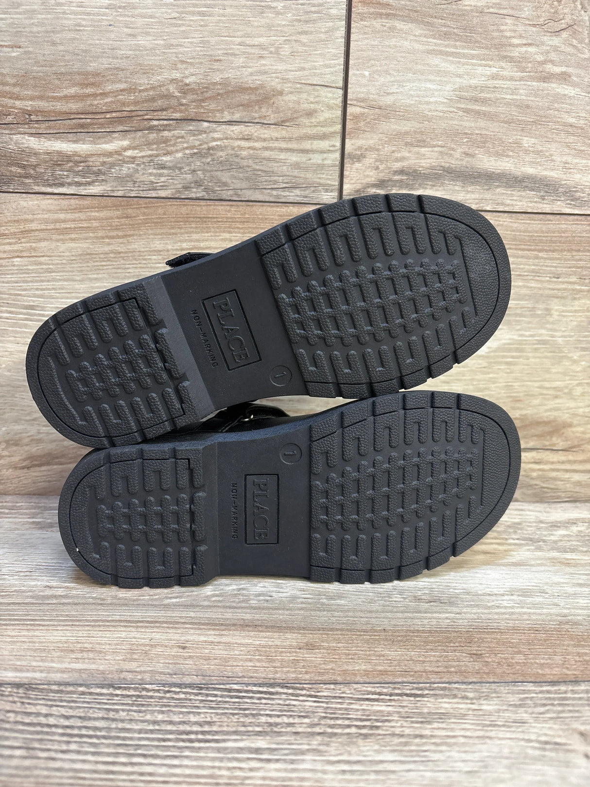 Bottom view of Children's Place black Mary Jane flats showing non-marking rubber soles with tread and 'PLACE' logo