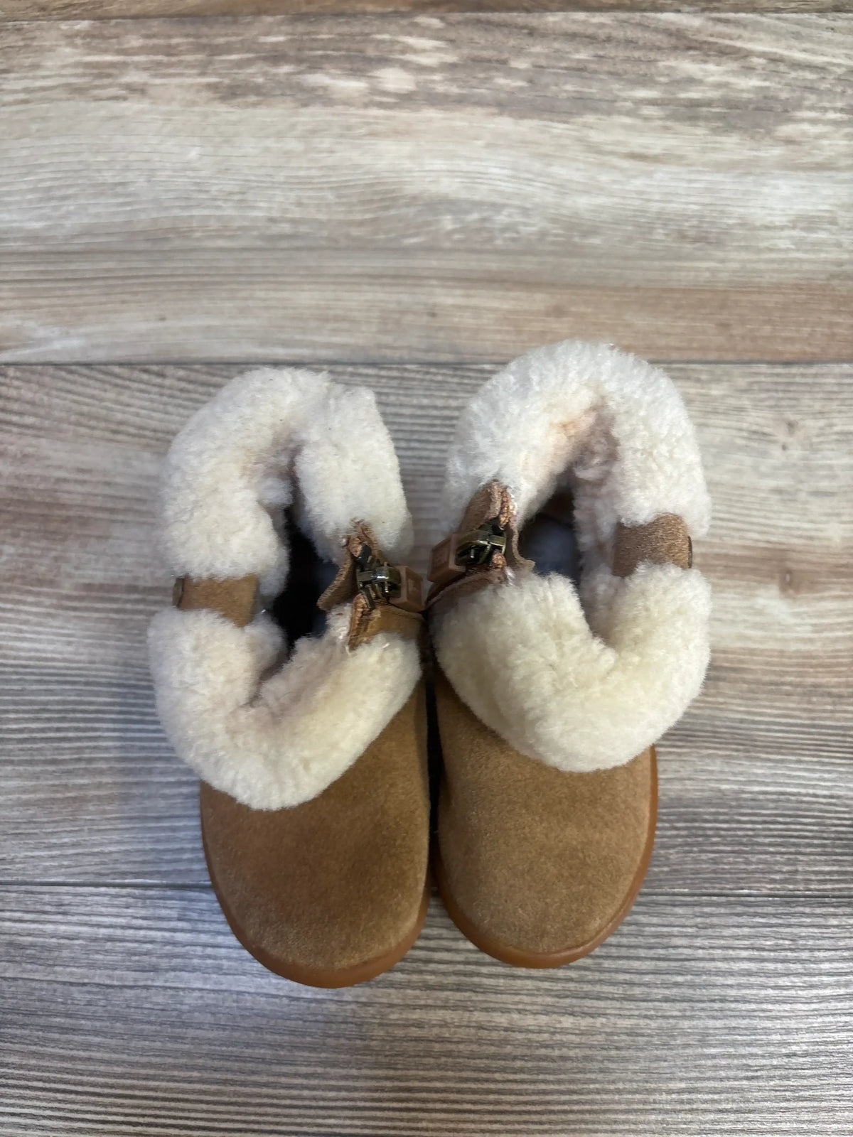 Top view of UGG Ramona toddler chestnut suede boots showcasing folded cuff with white shearling lining and buckle on wood floor