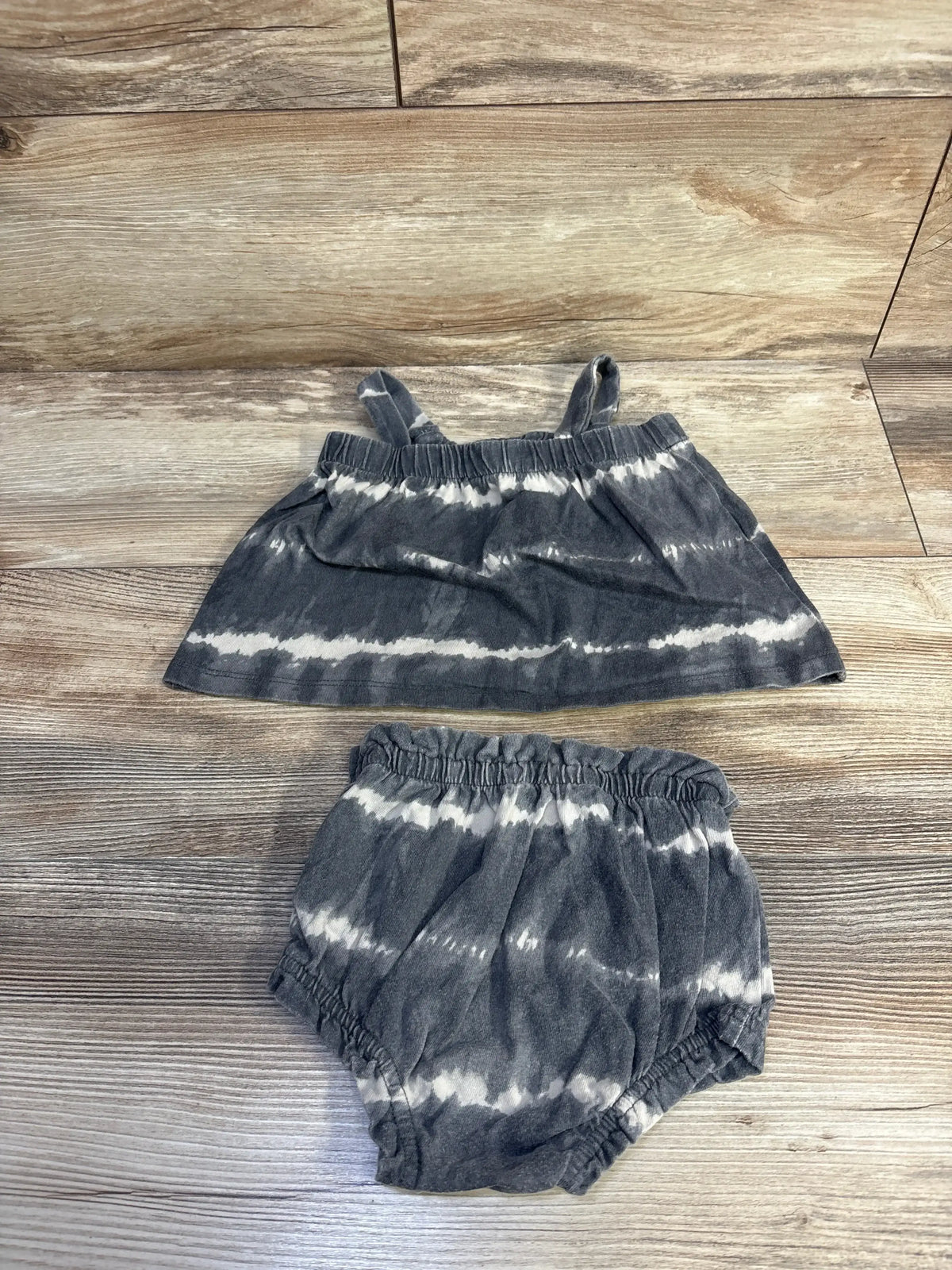Top-down view of Baby Gap 2pc organic tie-dye outfit set showcasing tank top and shorts with ruffled elastic edges on a wood-look floor