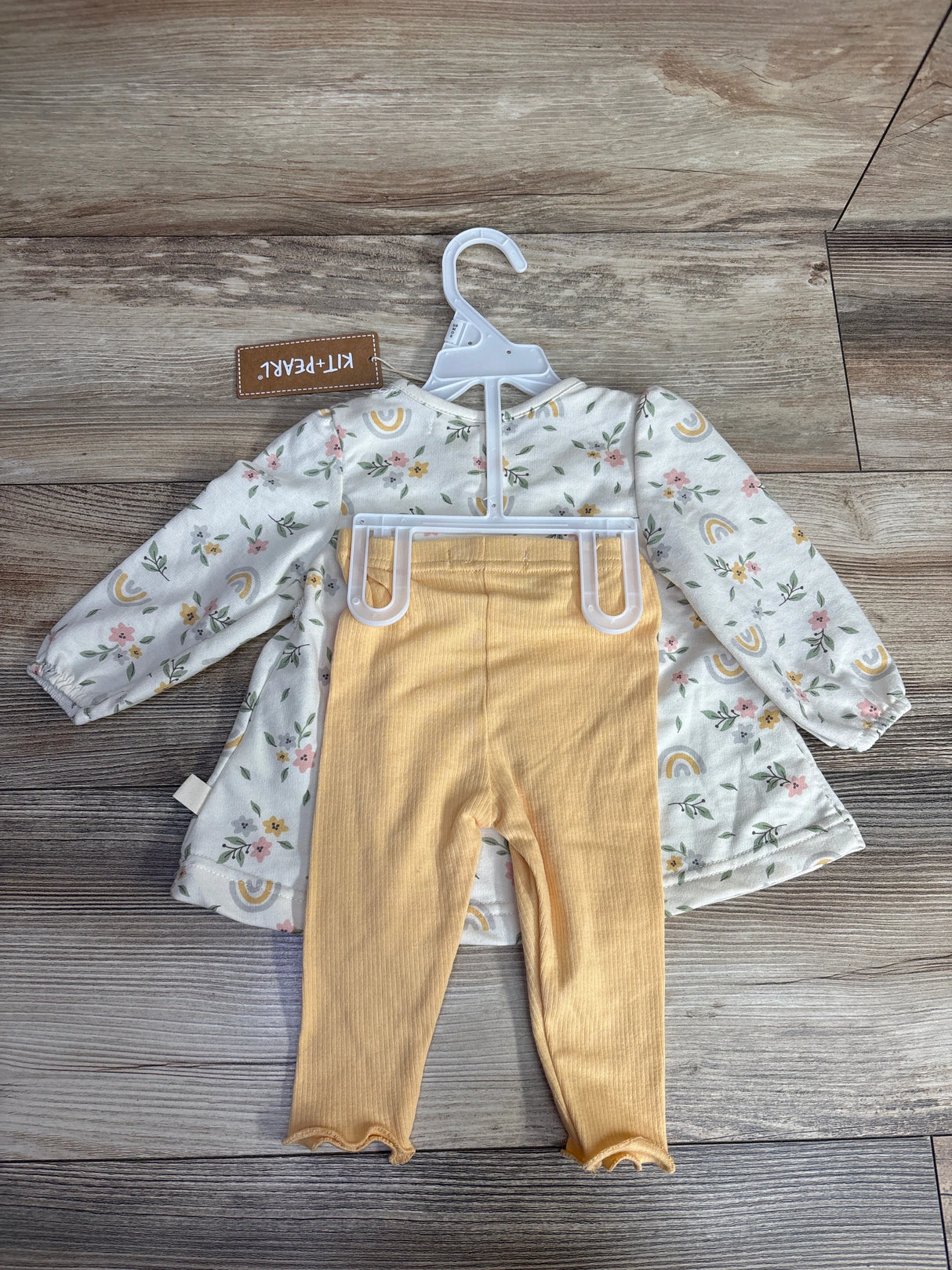 Baby outfit with floral long-sleeve dress and yellow ribbed leggings on hanger on wood floor