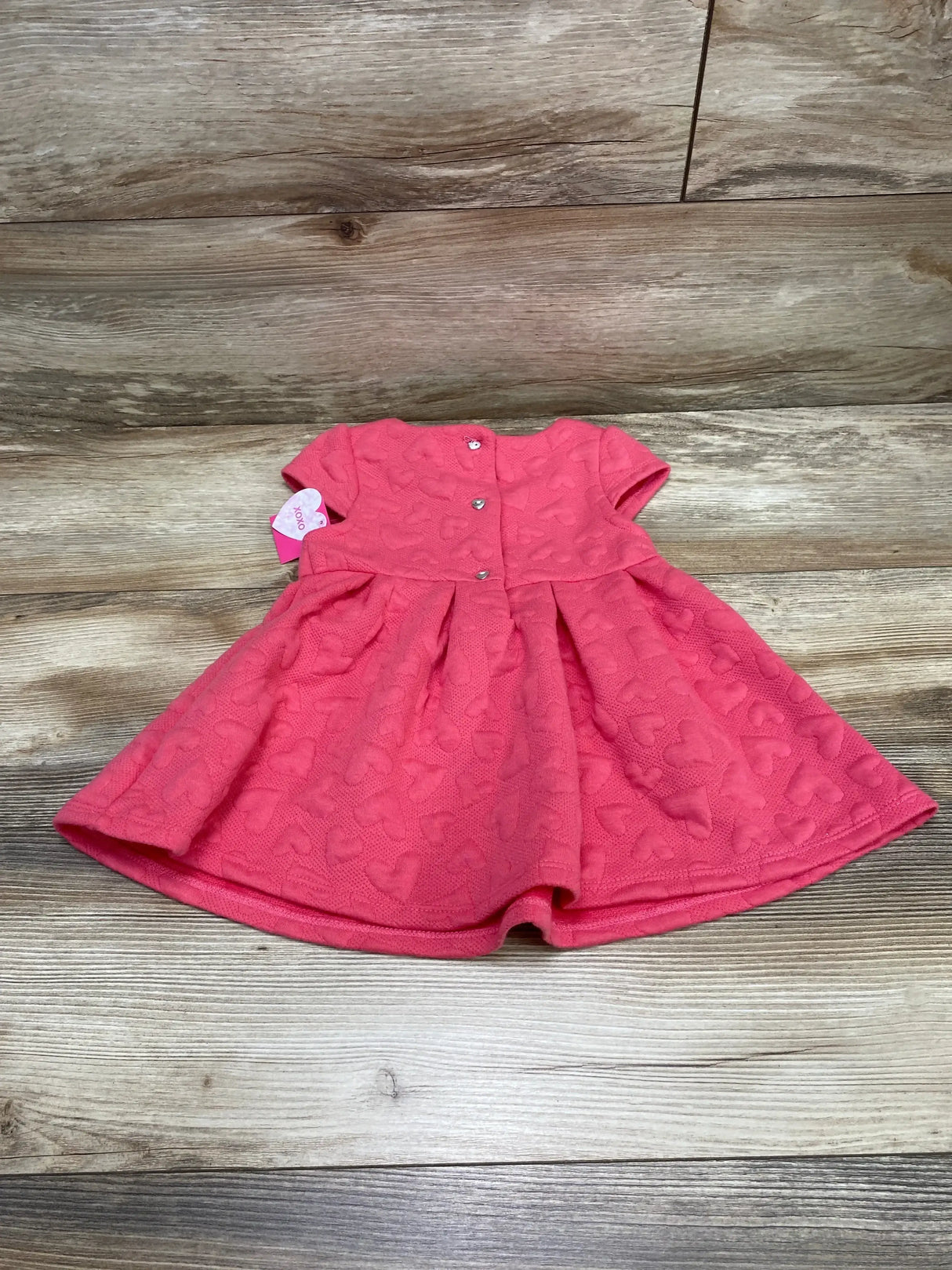 Flat lay of pink Isaac Mizrahi toddler dress (3T) showing quilted heart texture and front snap buttons on wood background