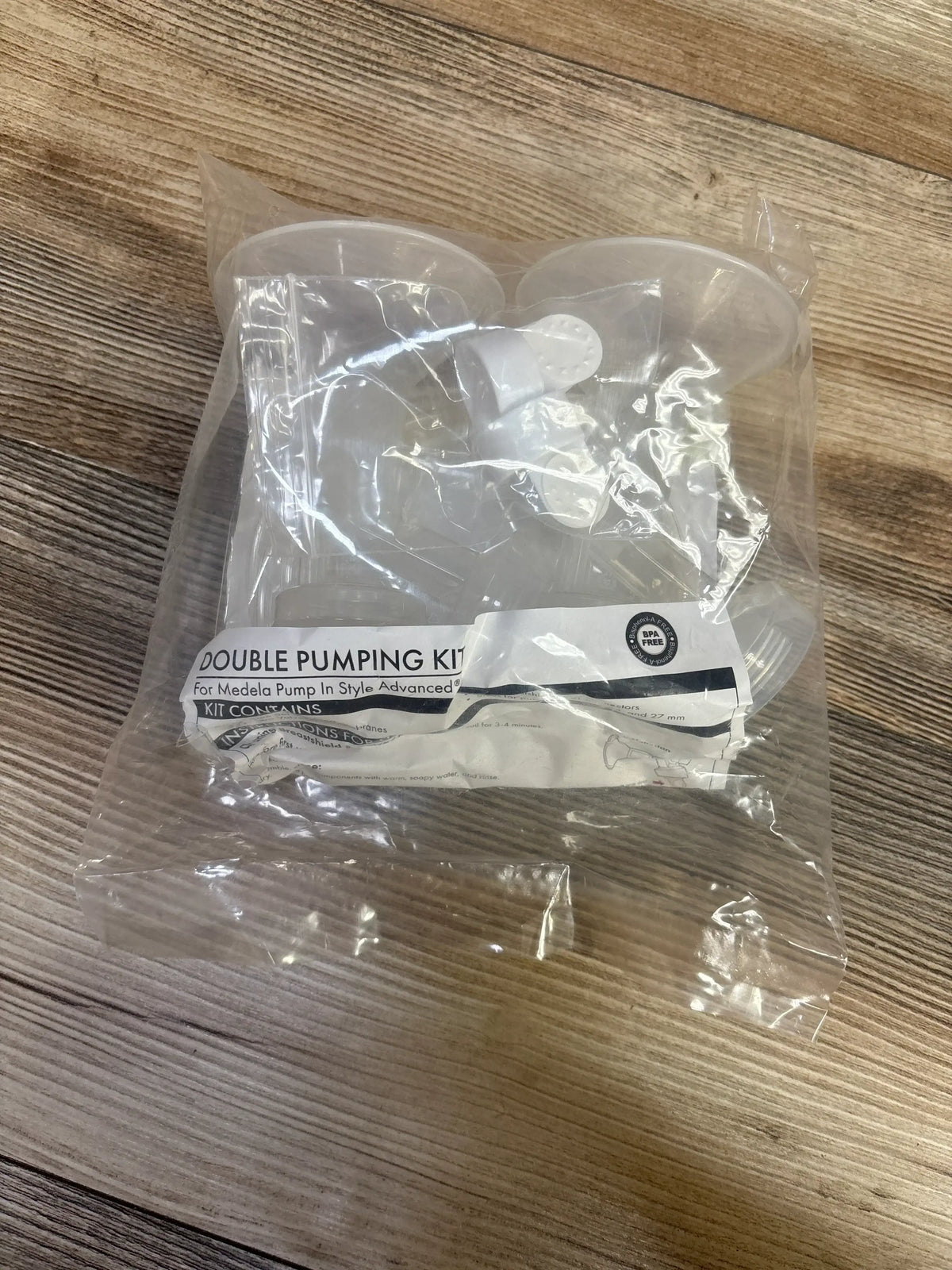 Top view of new Medela double pumping kit for Pump In Style Advanced in sealed clear bag with white label on wood floor
