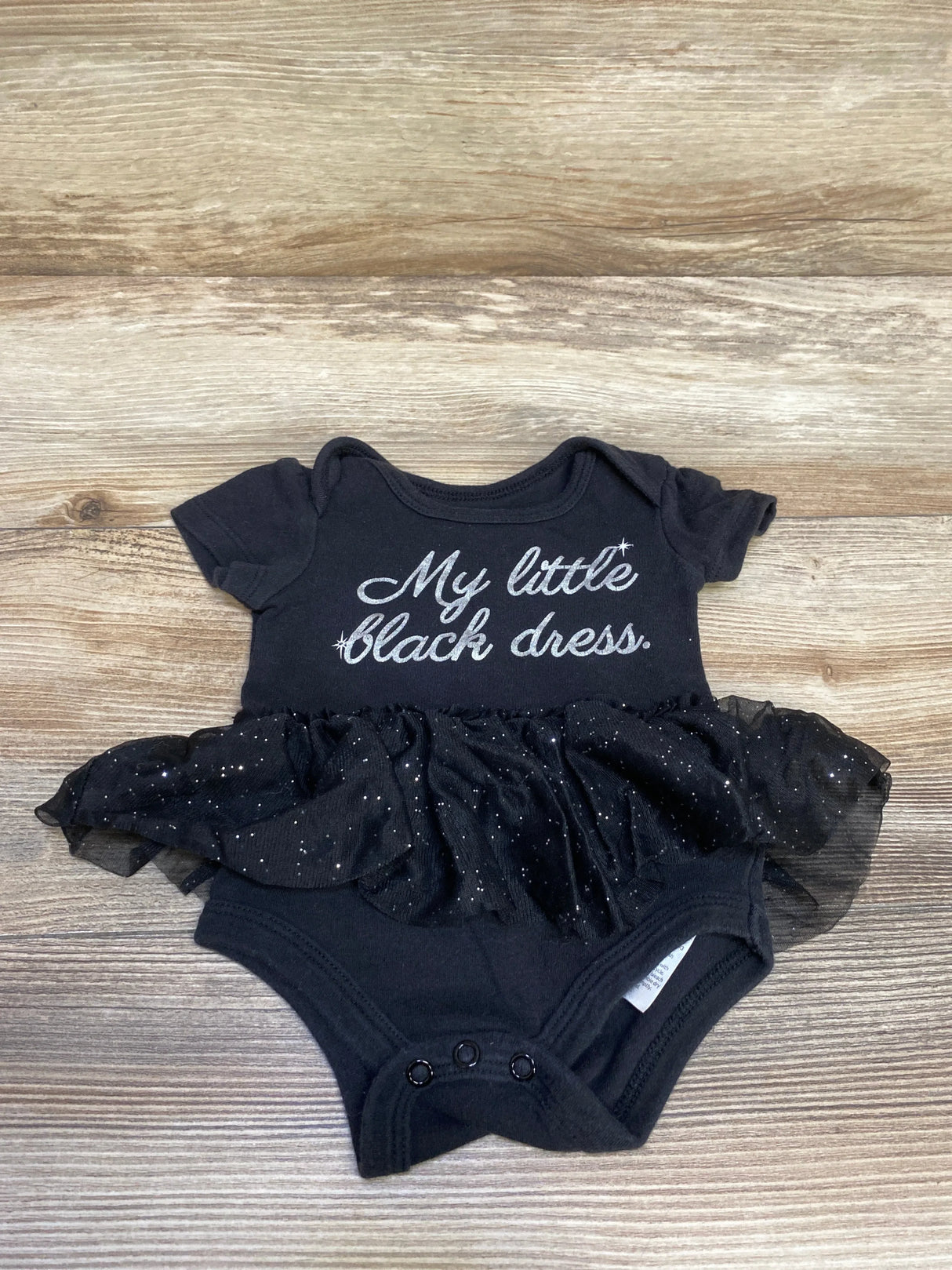 Black baby onesie with sparkly tutu and glitter text reading 'My little black dress' on wooden background