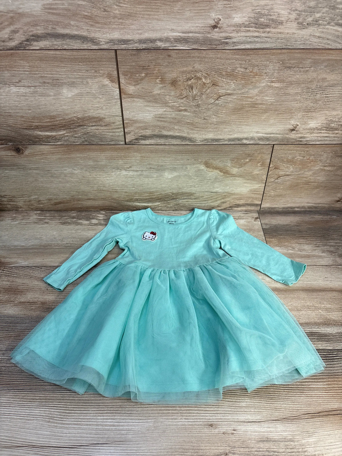 Front view of Carter’s Hello Kitty long sleeve tulle dress in teal with full tulle skirt and character design on wood flooring