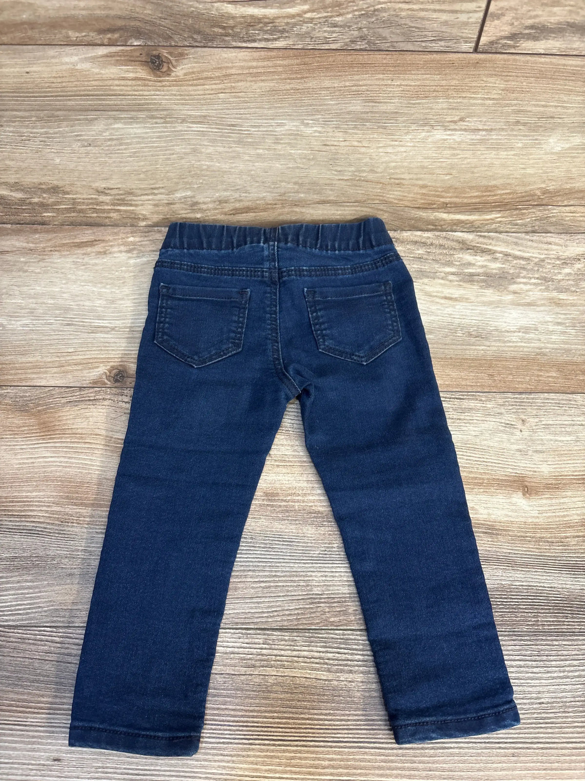 Flat lay of OshKosh navy toddler pull-on denim jeggings size 18m showing elastic pull-on waist and slim legs on wood floor
