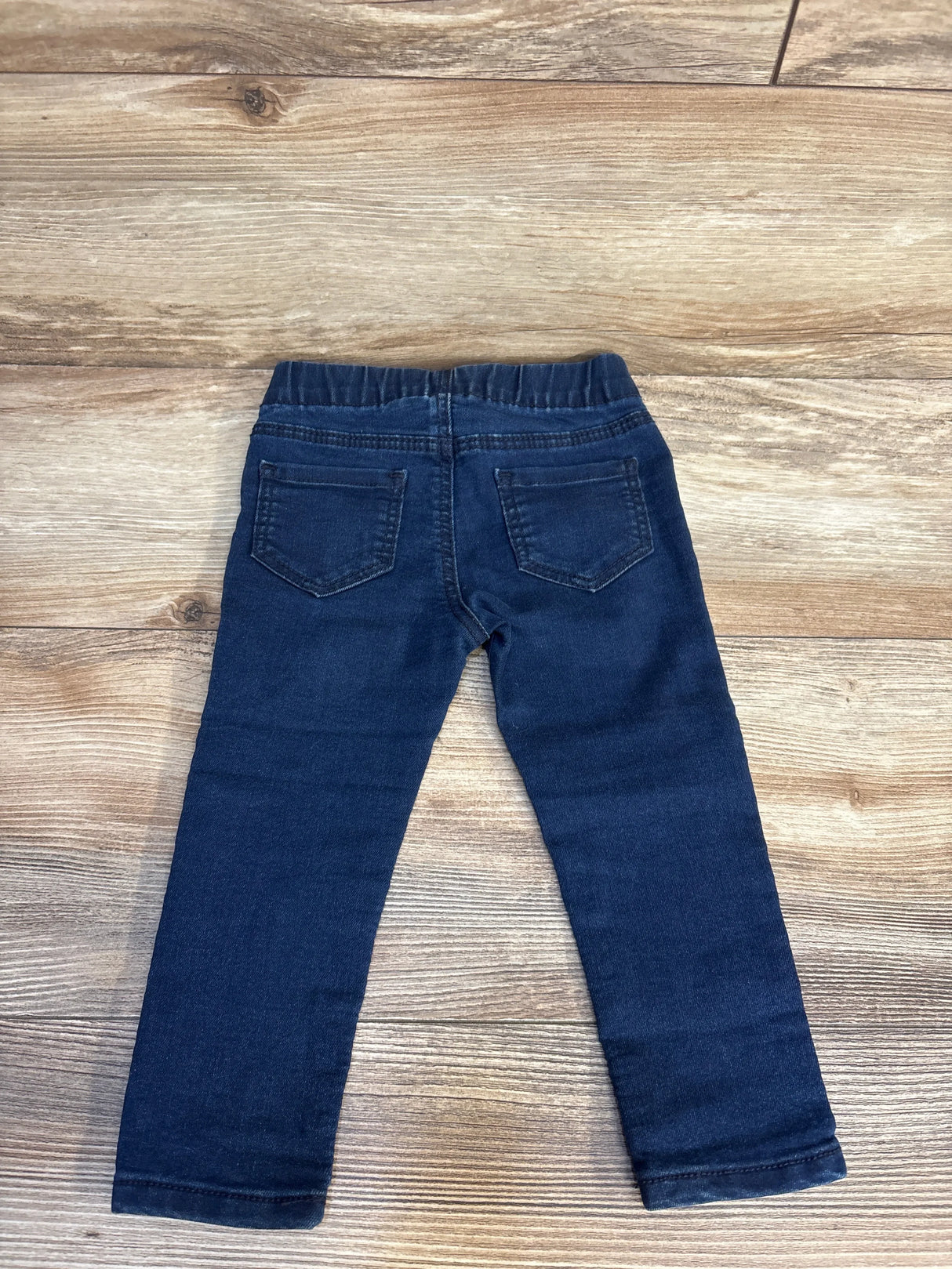 Back view of OshKosh navy pull-on denim jeggings size 18 months showing elastic waistband and back pockets on wood floor