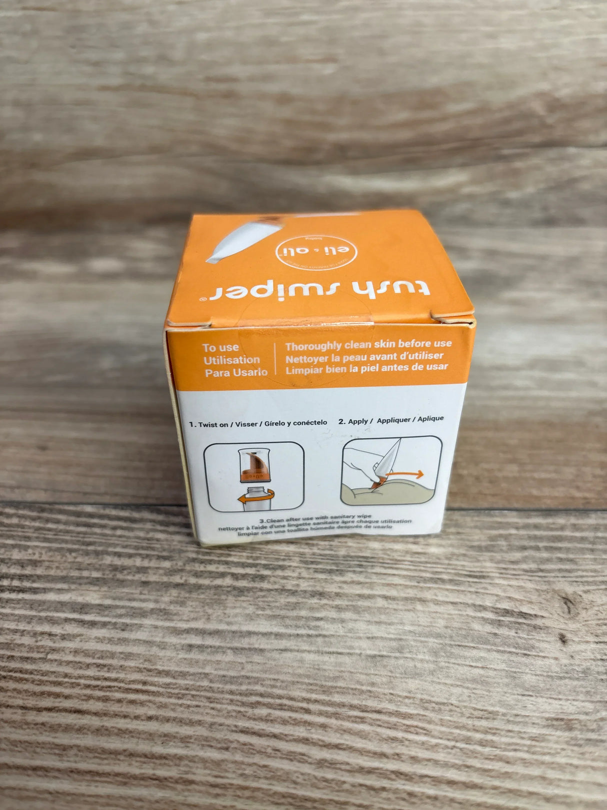 Front view of Eli & Ali Tush Swiper cream applicator box showing illustrated usage steps and orange top on wooden surface