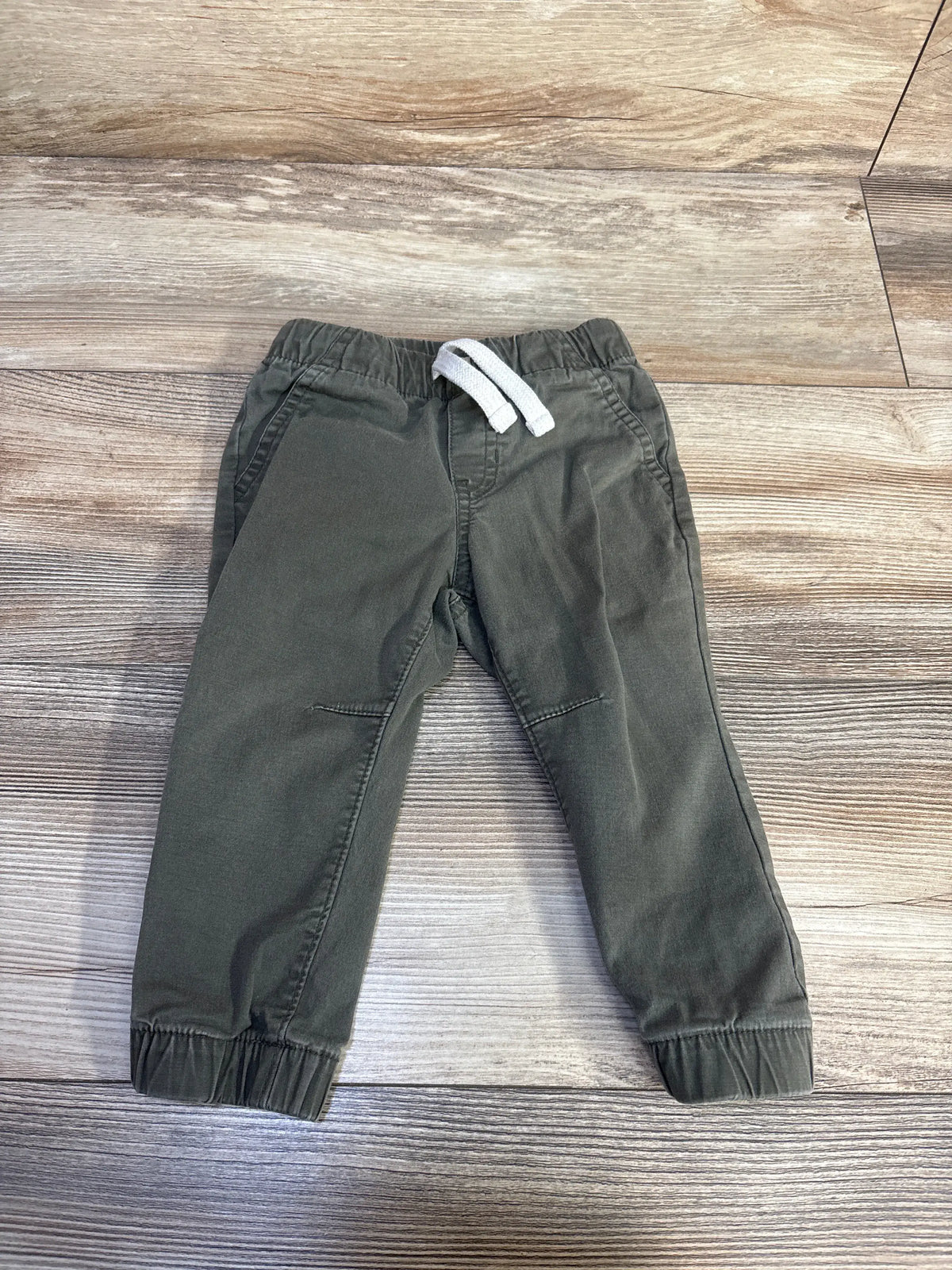 Front view of Cat & Jack green drawstring joggers showcasing an elastic waistband, side pockets, and ribbed cuffs on a wood-look floor