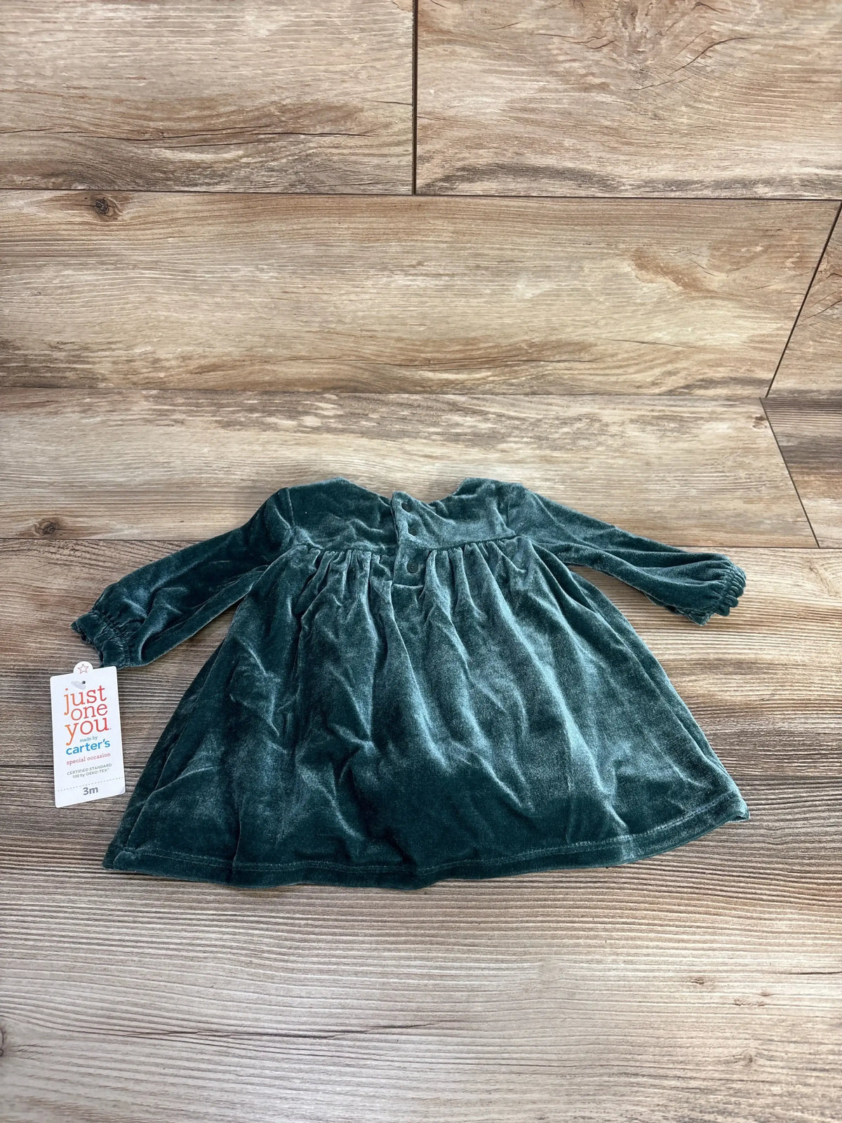 Flat lay of green velvet long sleeve bodysuit dress showing gathered skirt and snap closure with wood floor background