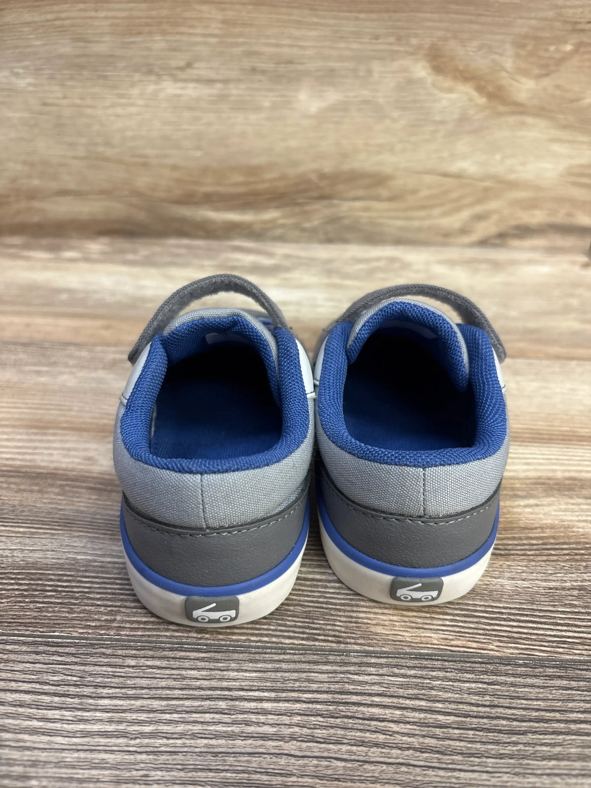 Rear view of See Kai Run Rory sneakers in grey and blue showcasing padded blue collars and heel graphics on a wood-look surface