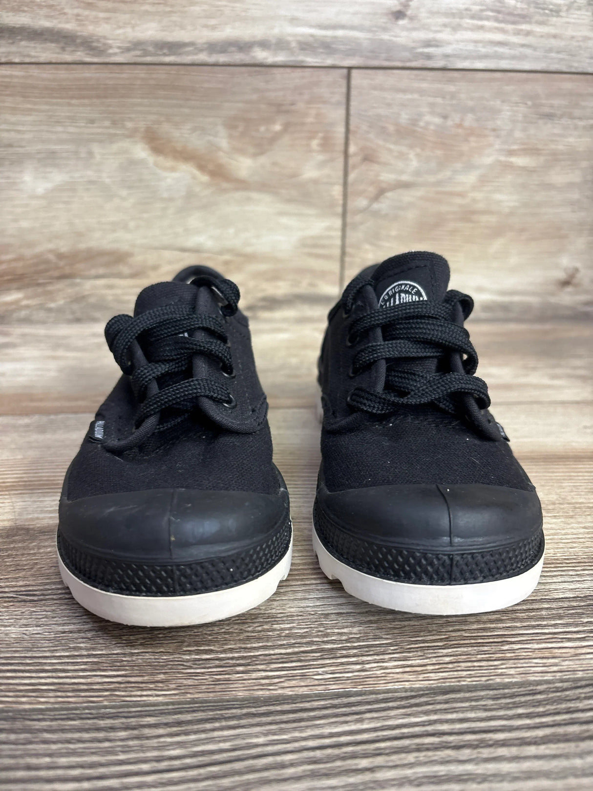 Pair of black canvas toddler sneakers with white soles on wooden floor background