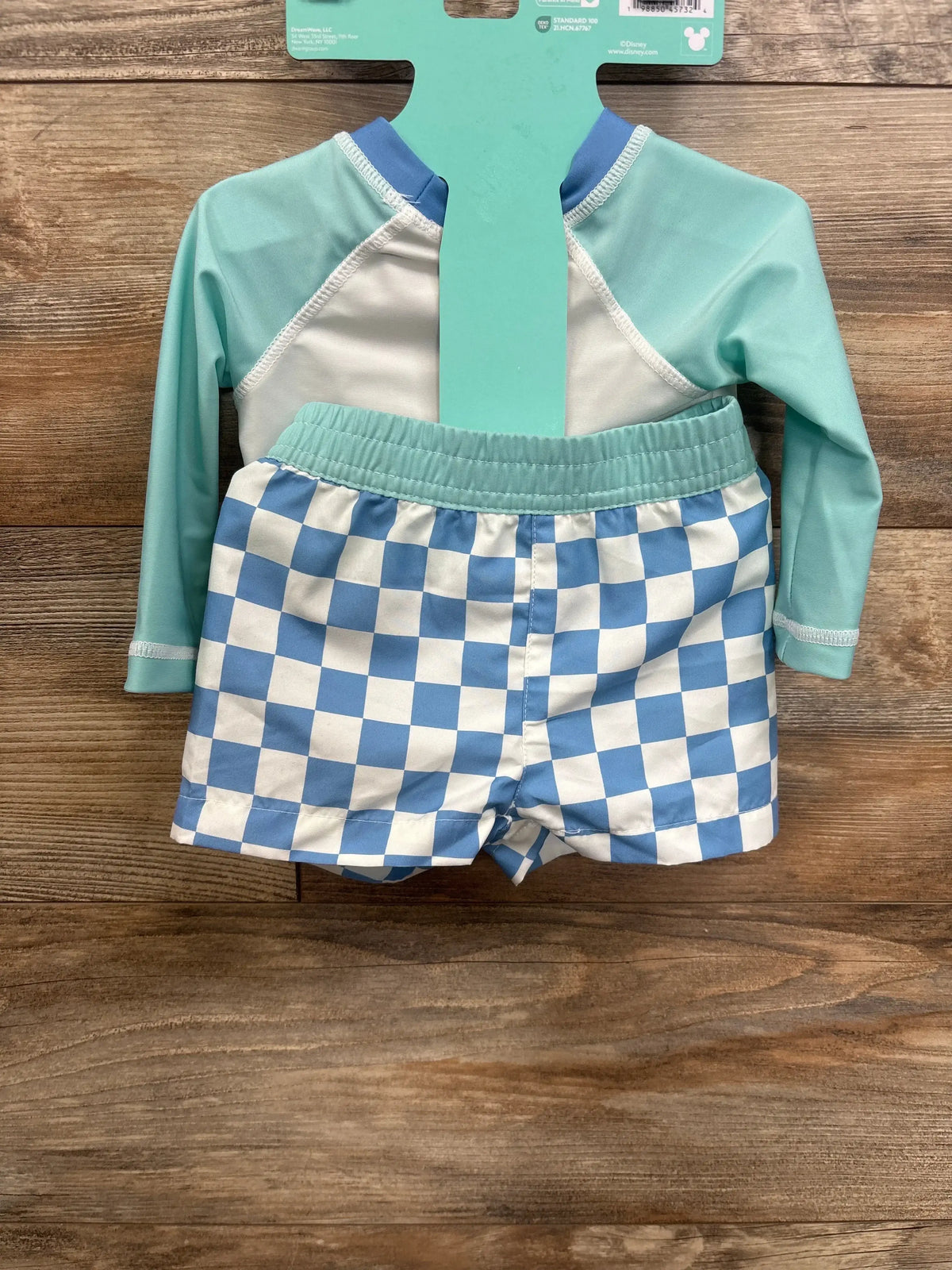 Kids long sleeve swim shirt and blue checkered swim trunks on wood background