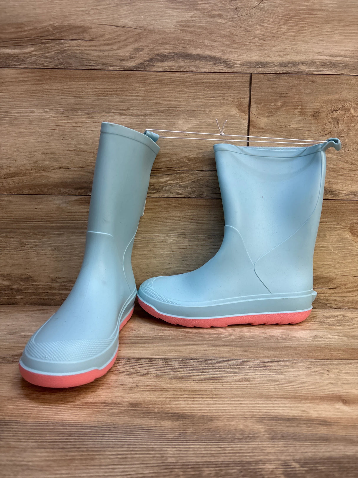 Light blue kids rain boots with pink soles on wooden background