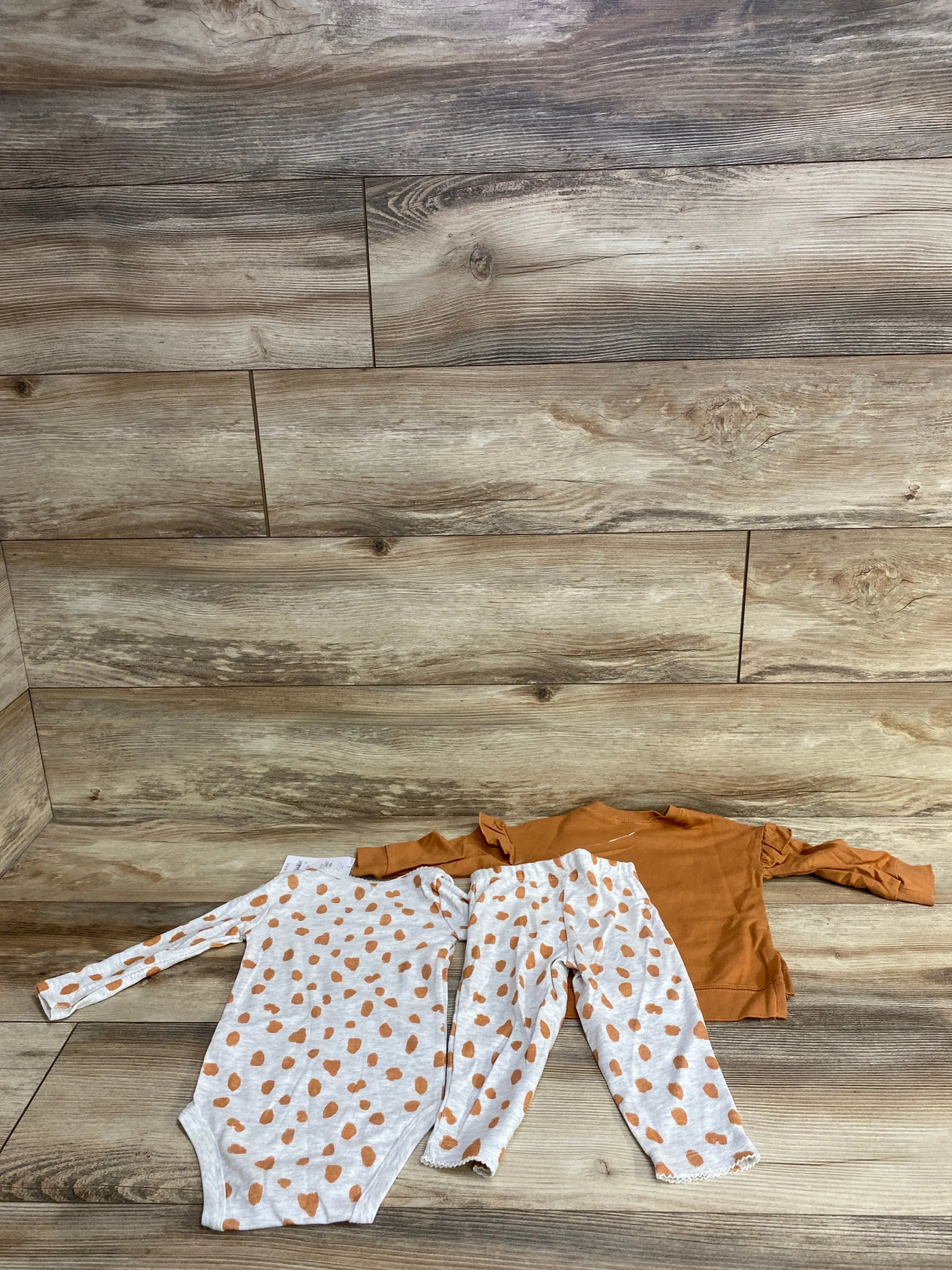Baby girl outfit set with polka dot bodysuit, matching pants, and orange top on wood floor
