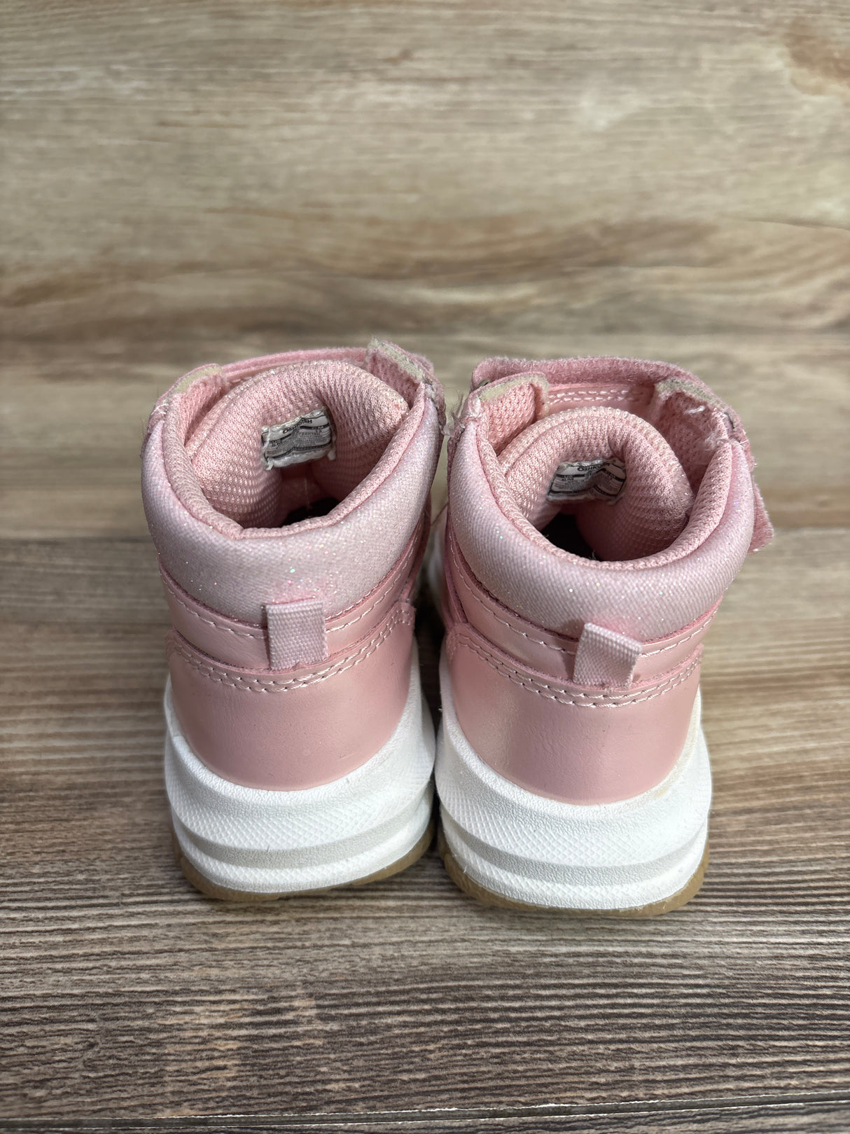 Pair of pink toddler high-top sneakers with white soles on wooden surface
