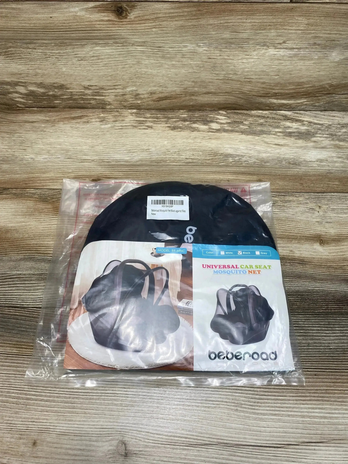 Top down view of Beberoad car seat mosquito net in black, folded in round pouch inside clear plastic packaging on wood surface