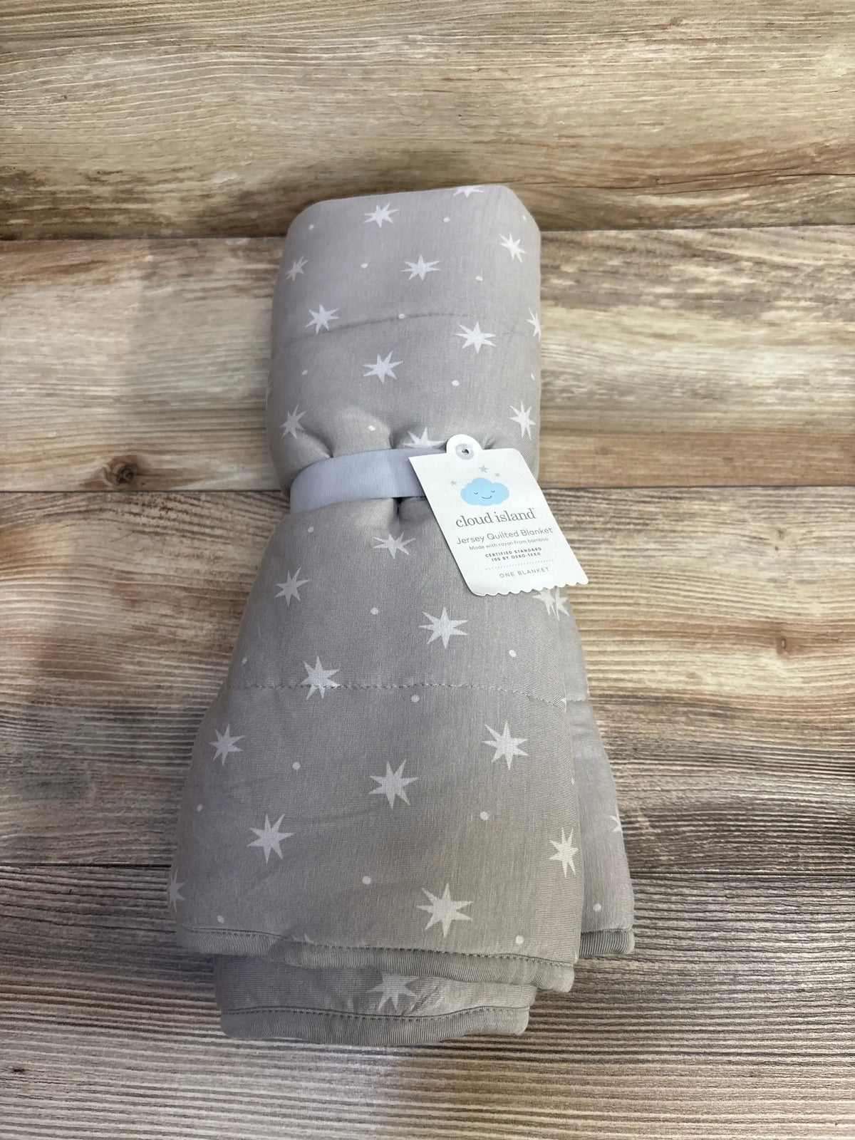 Top-down view of folded Cloud Island quilted baby blanket, grey with white star print, tied with band on wood background