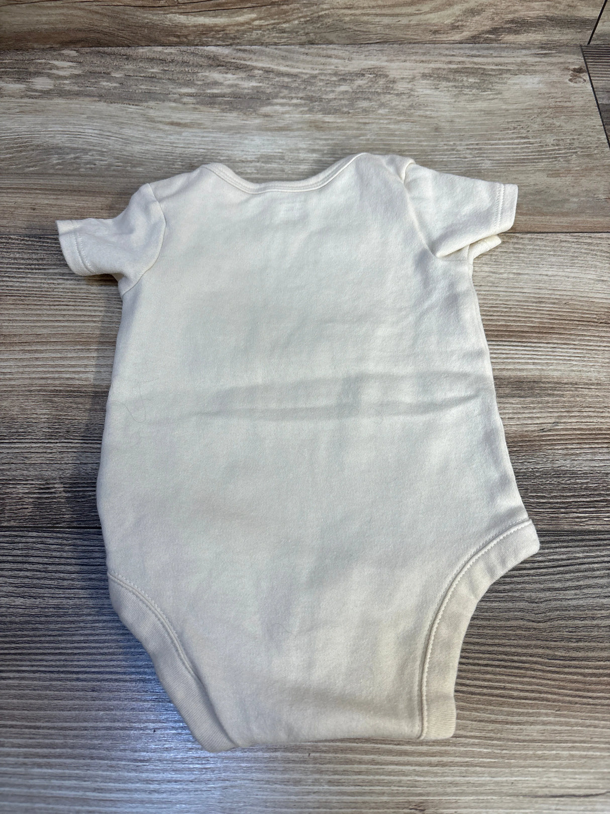 Plain white baby bodysuit with short sleeves on wood floor, gently used kids clothing.