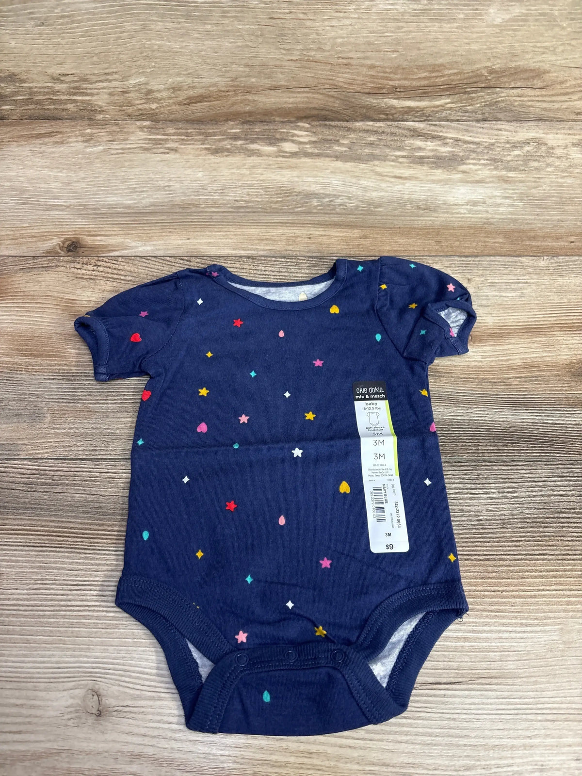 Navy blue baby onesie with colorful stars and hearts pattern, size 3M, on wooden surface