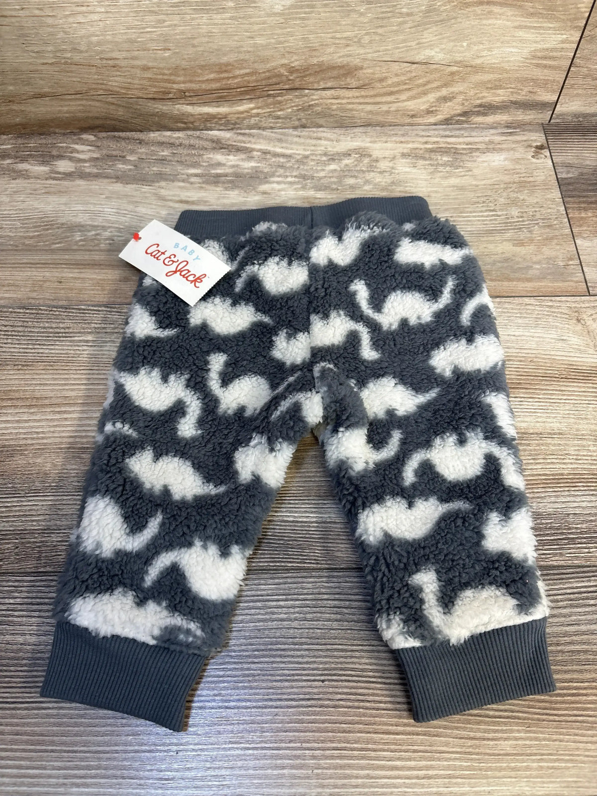 Fuzzy gray and white baby pants with dinosaur print and ribbed cuffs on wood floor