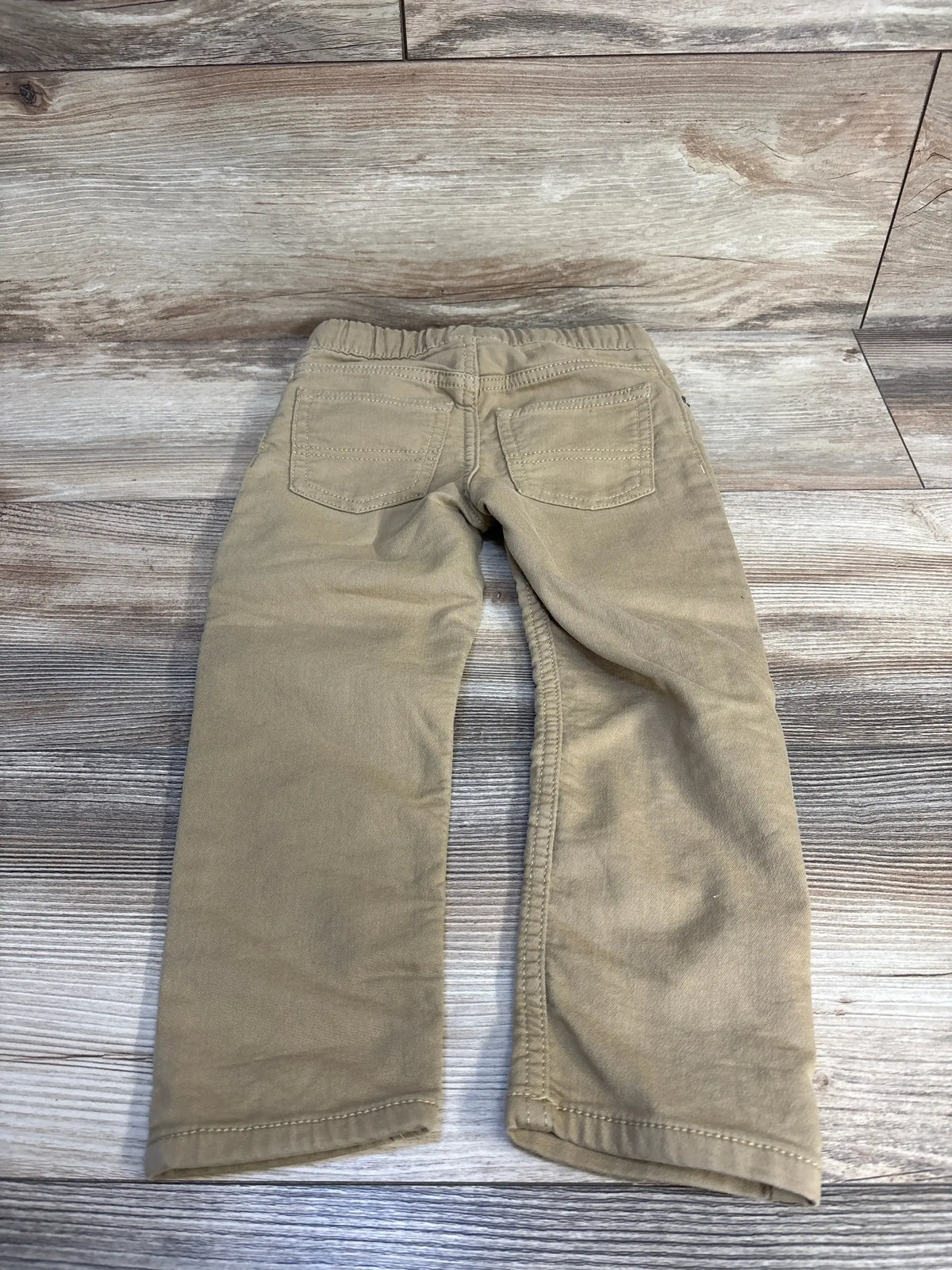 Back view of Oshkosh drawstring joggers in wheat tan showcasing elastic waist and back pockets flat lay on wood plank floor