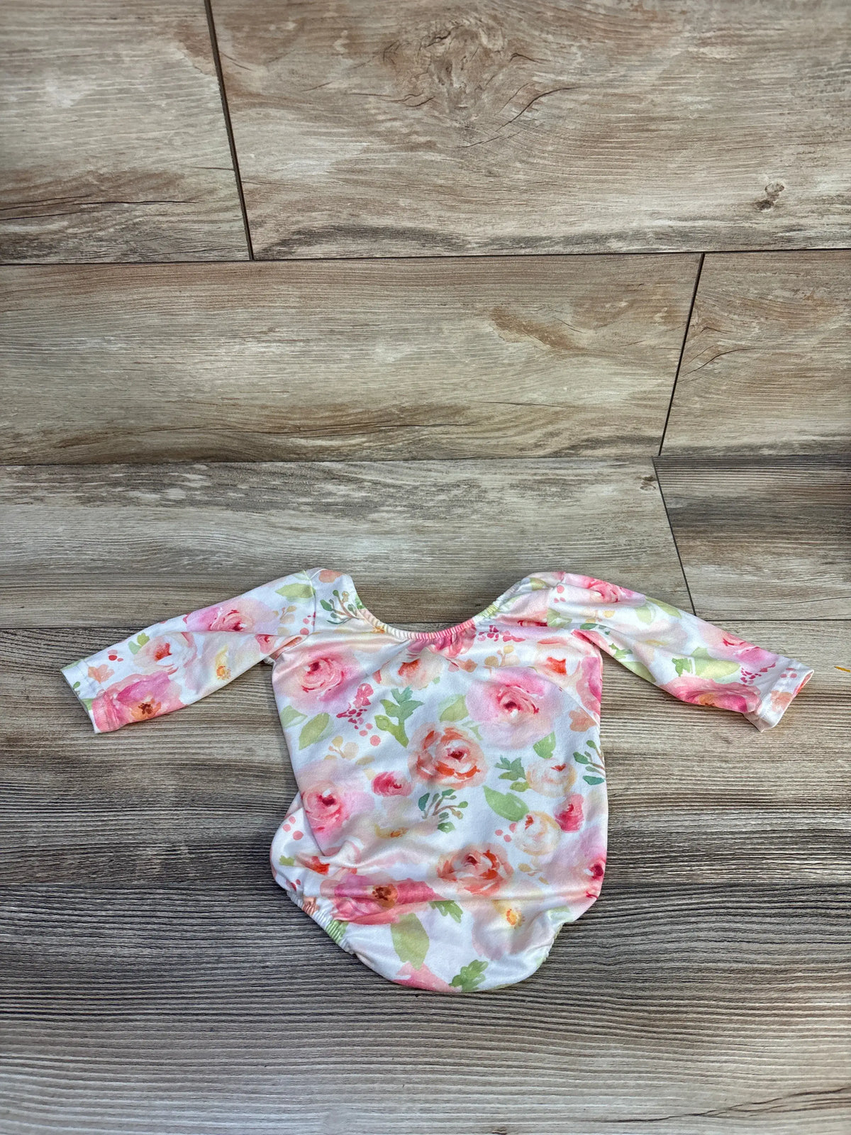Front view of Castle Rose Boutique white floral leotard for 3 to 6 months, with long sleeves, on a wood background