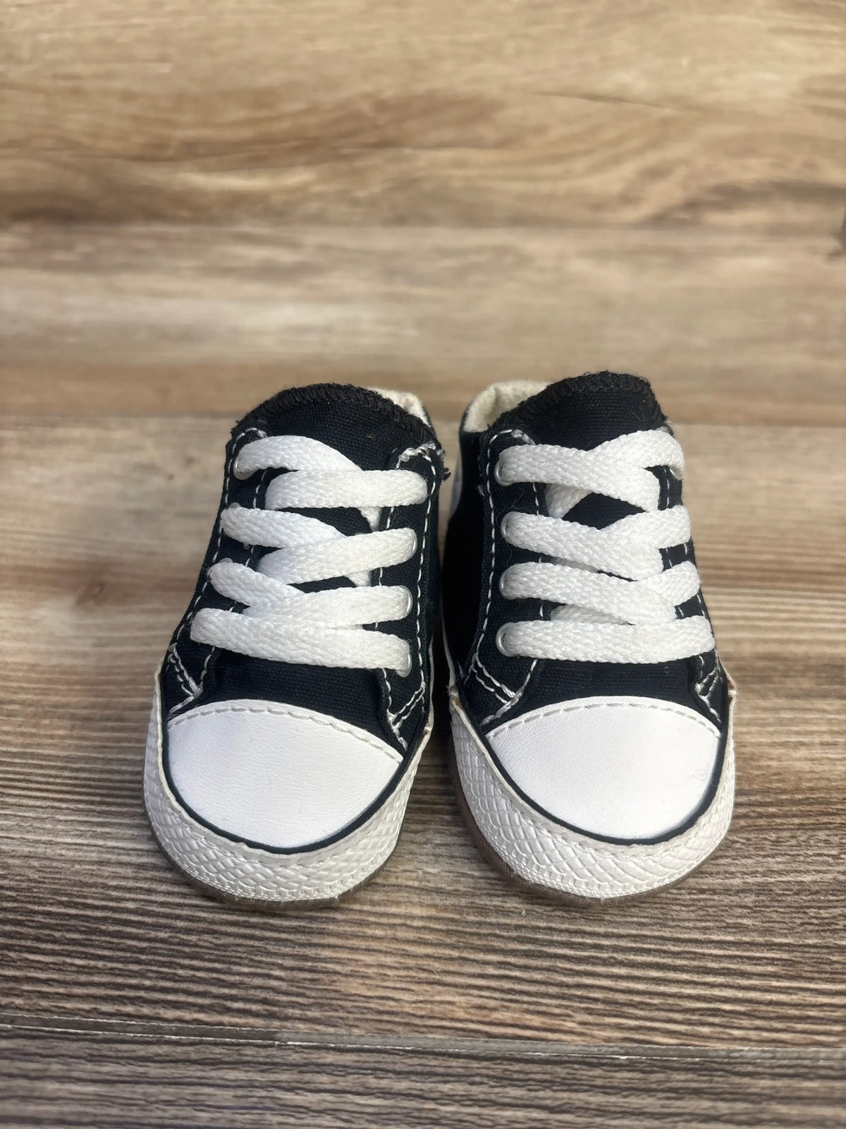 Front view of black Converse All Star Cribster Easy-On Shoes with white laces, toe caps, and soles on a wood surface