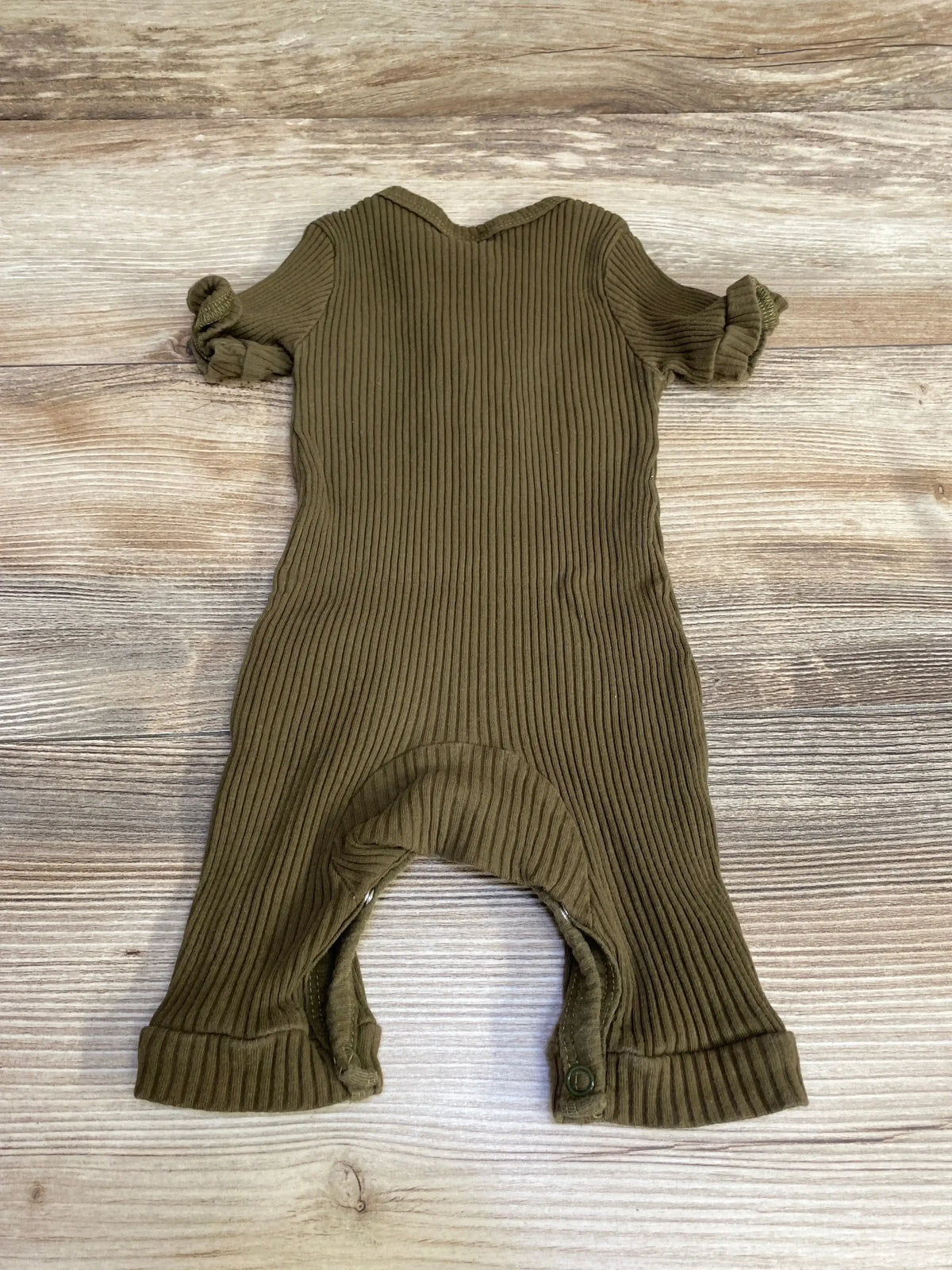 Flat lay of olive green ribbed Henley baby romper showing V-neck, short rolled sleeves, snap crotch and cuffed legs on wood background