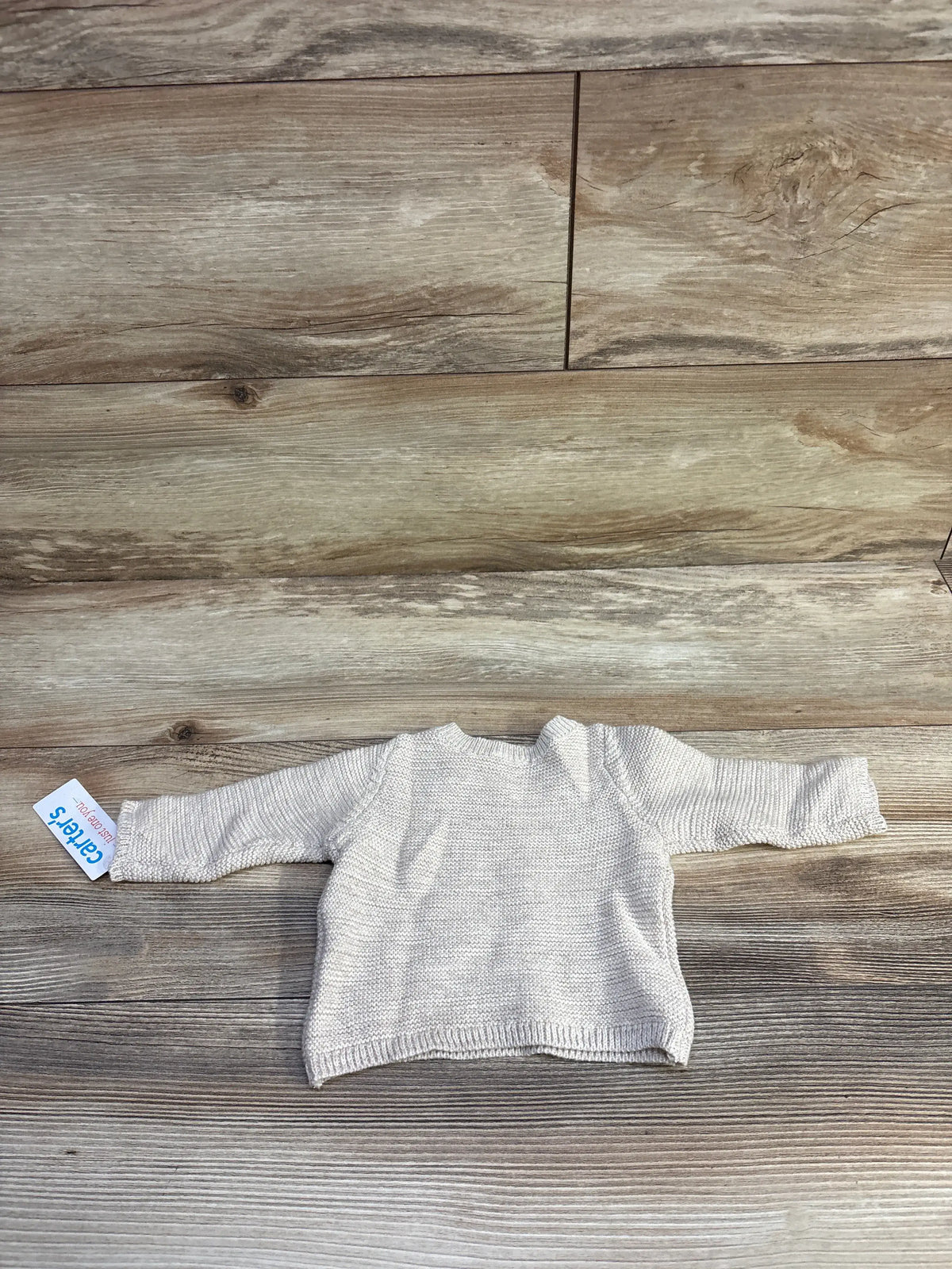 Flat lay of newborn beige knit sweater showcasing knit texture, raglan long sleeves and ribbed hem on wood background