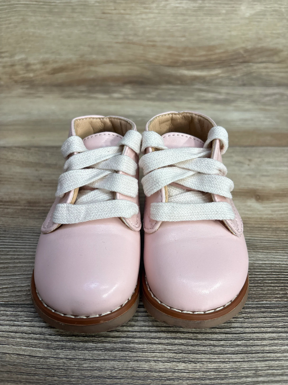Front view of Josmo First Walker ankle baby shoes, pink leather, showing white laces, toe and stitched brown sole on wood