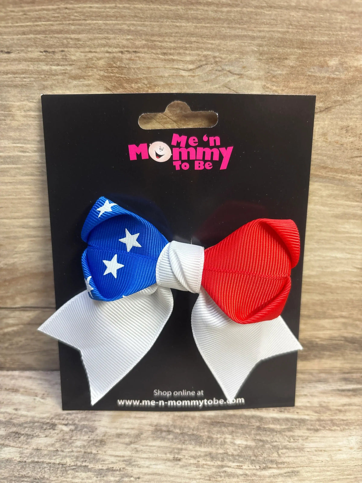 Front view of American flag hair bow showcasing blue star-patterned loop, red loop, and white tails on black display card with Me n Mommy To Be logo