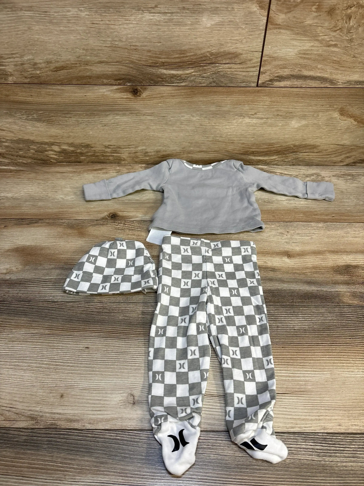 Gray and white checkered baby outfit set with hat, long sleeve top, and footed pants on wood floor