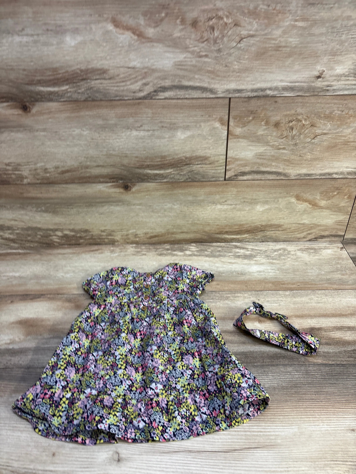 Flat lay of navy floral baby dress and matching headband showing puff sleeves and gathered waist on wood background