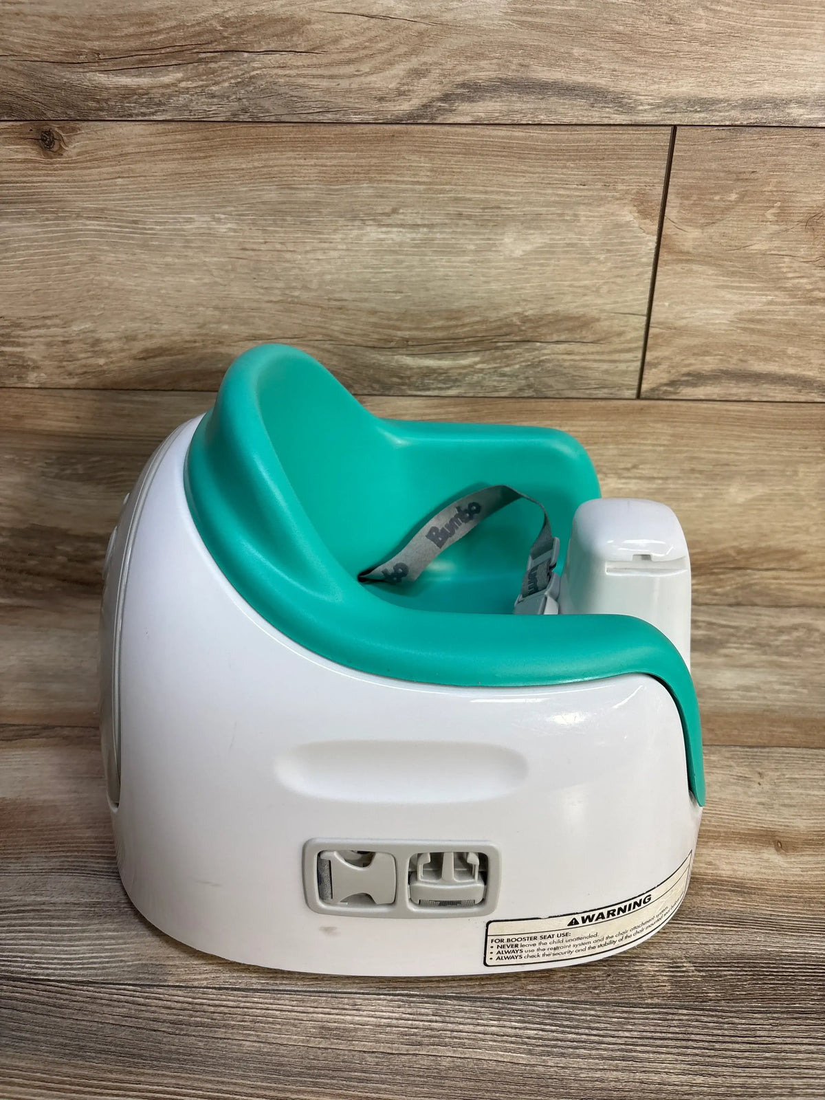 Side view of Bumbo Multi Seat with Removable Tray showcasing teal seat, white base, and safety harness on a wood floor