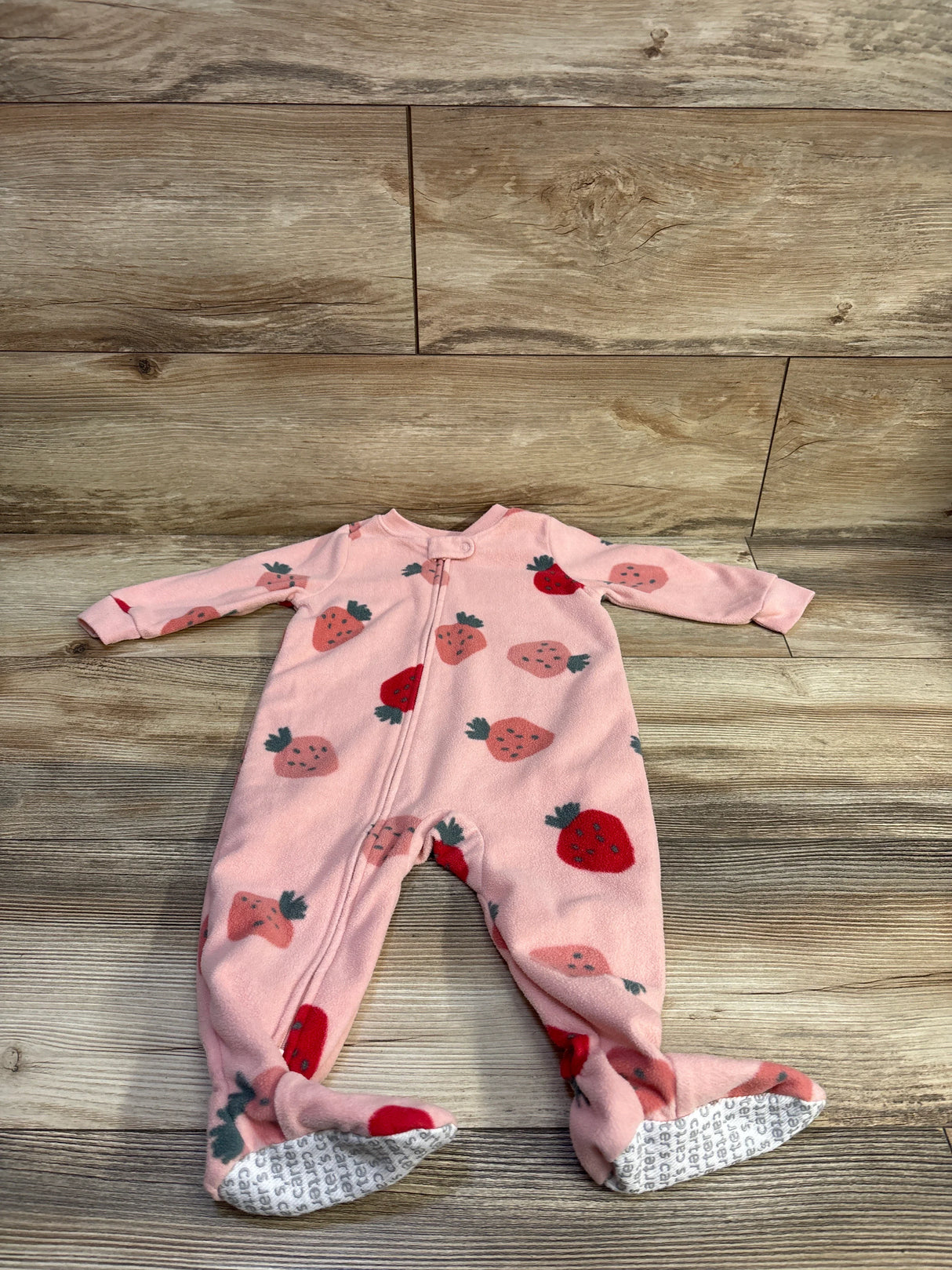 Flat lay view of Carter’s strawberry sleeper showing full length zipper, footed legs, strawberry print on wood floor