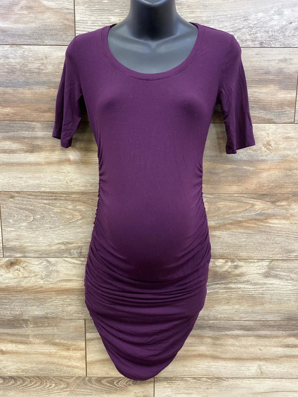 Front view of purple Motherhood Maternity bodycon dress with ruched sides and fitted silhouette on black mannequin with wood backdrop