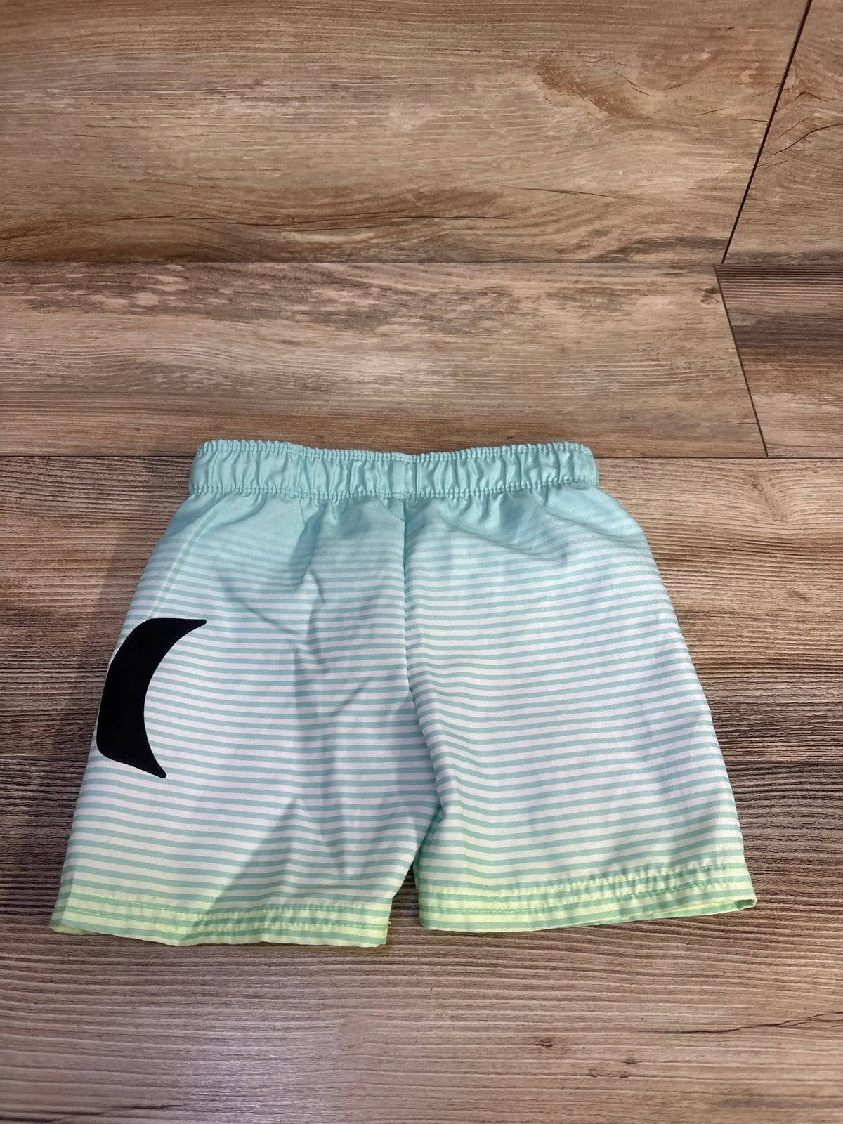 Top view of Hurley pull-on swim trunks in light blue and mint stripes showing black logo on wood floor
